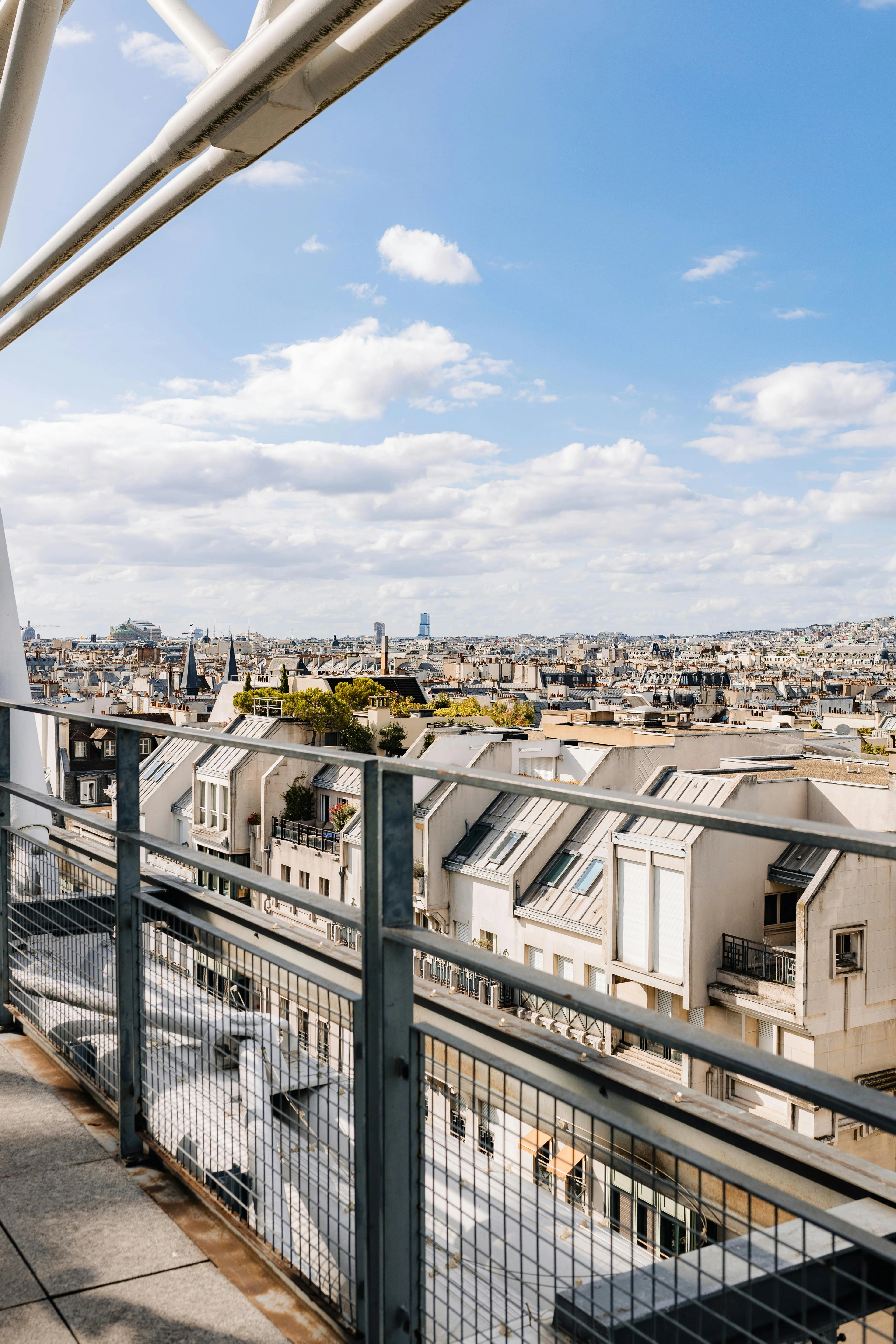 Scenic panoramic view of Paris rooftops and skyline from the Centre Pompidou, with a clear blue sky and scattered clouds.