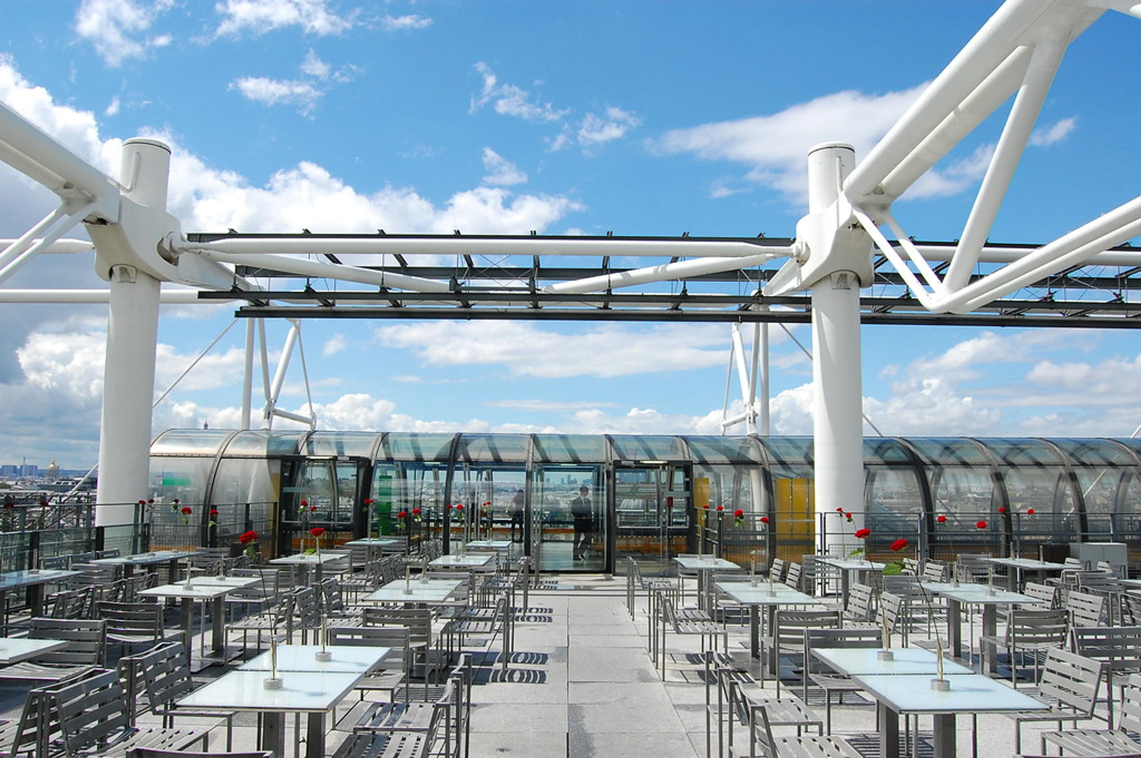 Uitzicht op het dakterras van het Centre Georges Pompidou in Parijs, met tafels en stoelen opgesteld voor buiten dineren, onder een blauwe lucht met witte wolken.