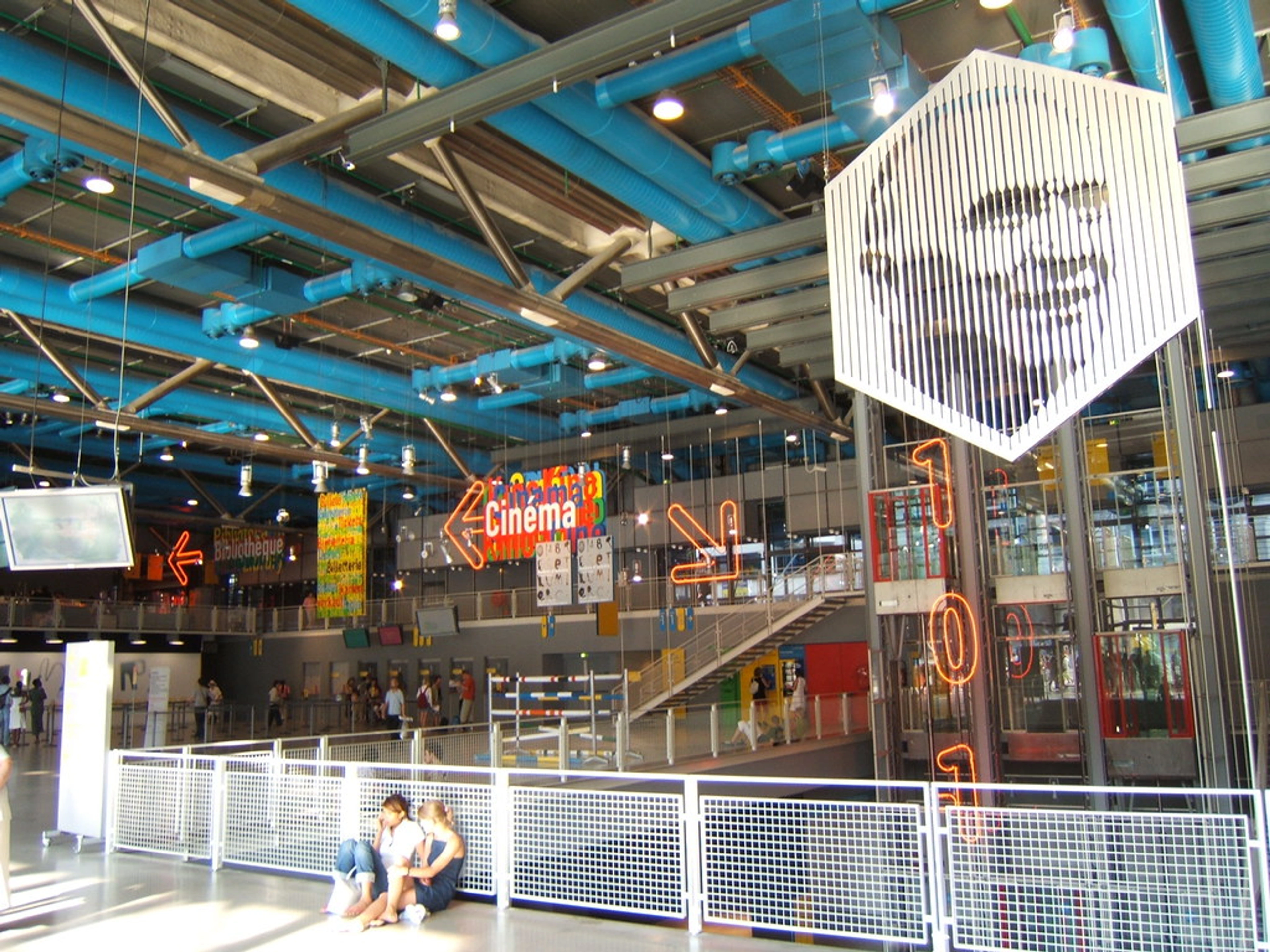 Interior view of the Centre Pompidou with a large hexagonal art installation hanging from the ceiling and colorful signage.