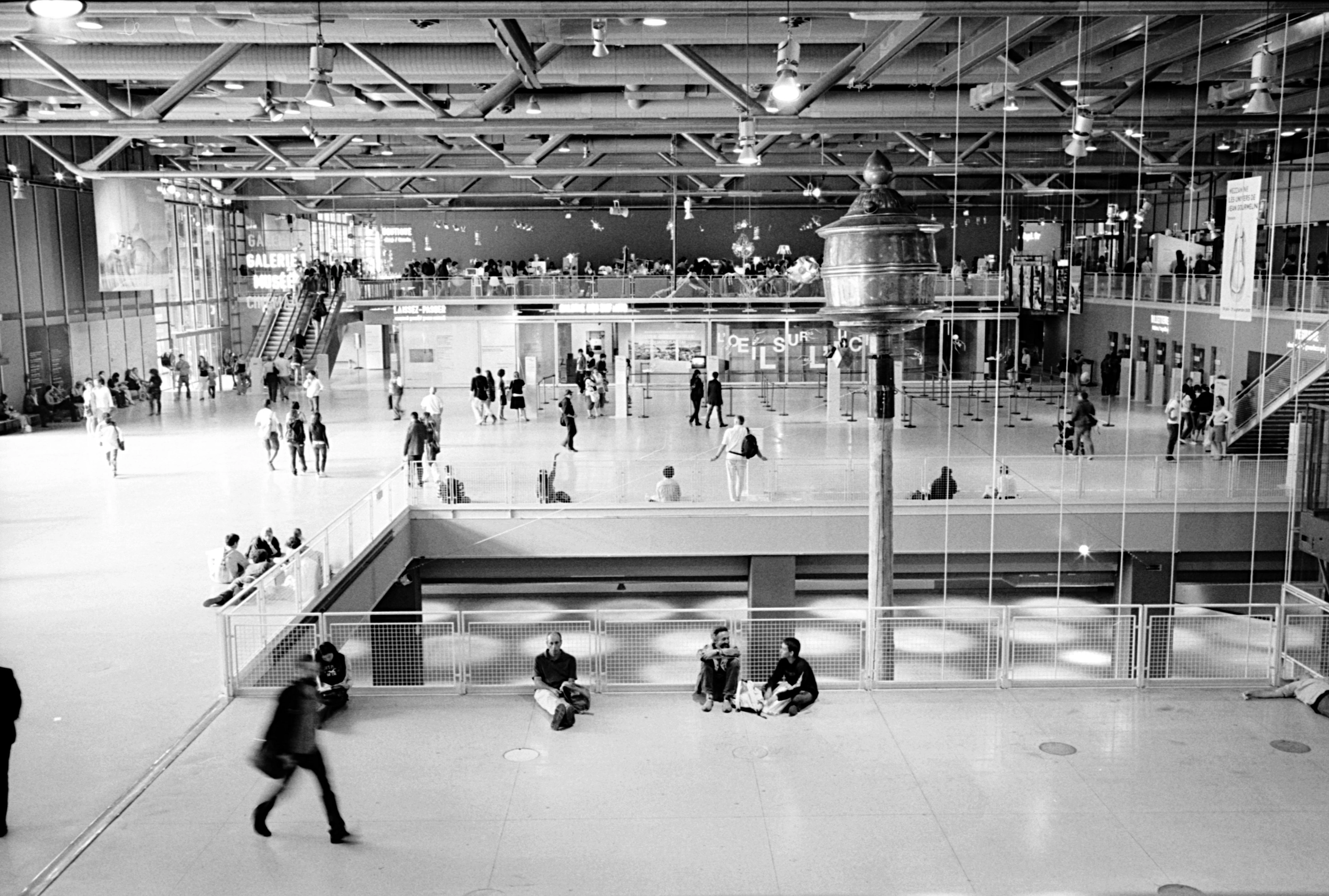 Interior view of the Centre Pompidou with visitors walking and sitting on the floor.