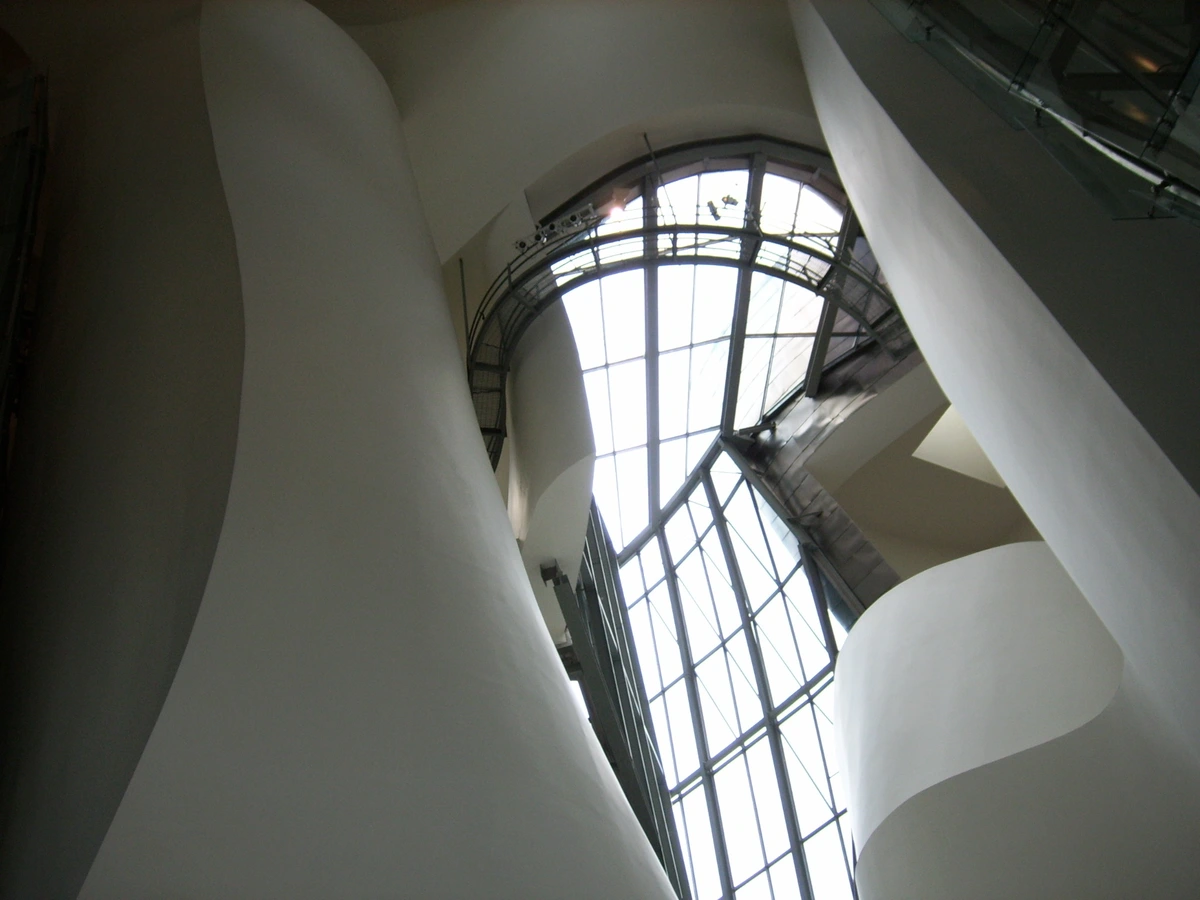 Interior view of the Guggenheim Museum Bilbao, showcasing its unique architecture with curved white walls and a large, arched window.