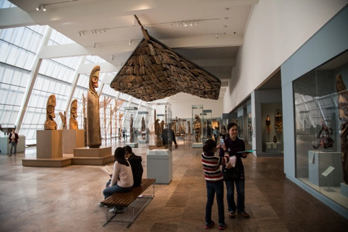 Metropolitan Museum of Art exhibit featuring tribal sculptures and artifacts under a large, textured ceiling installation.