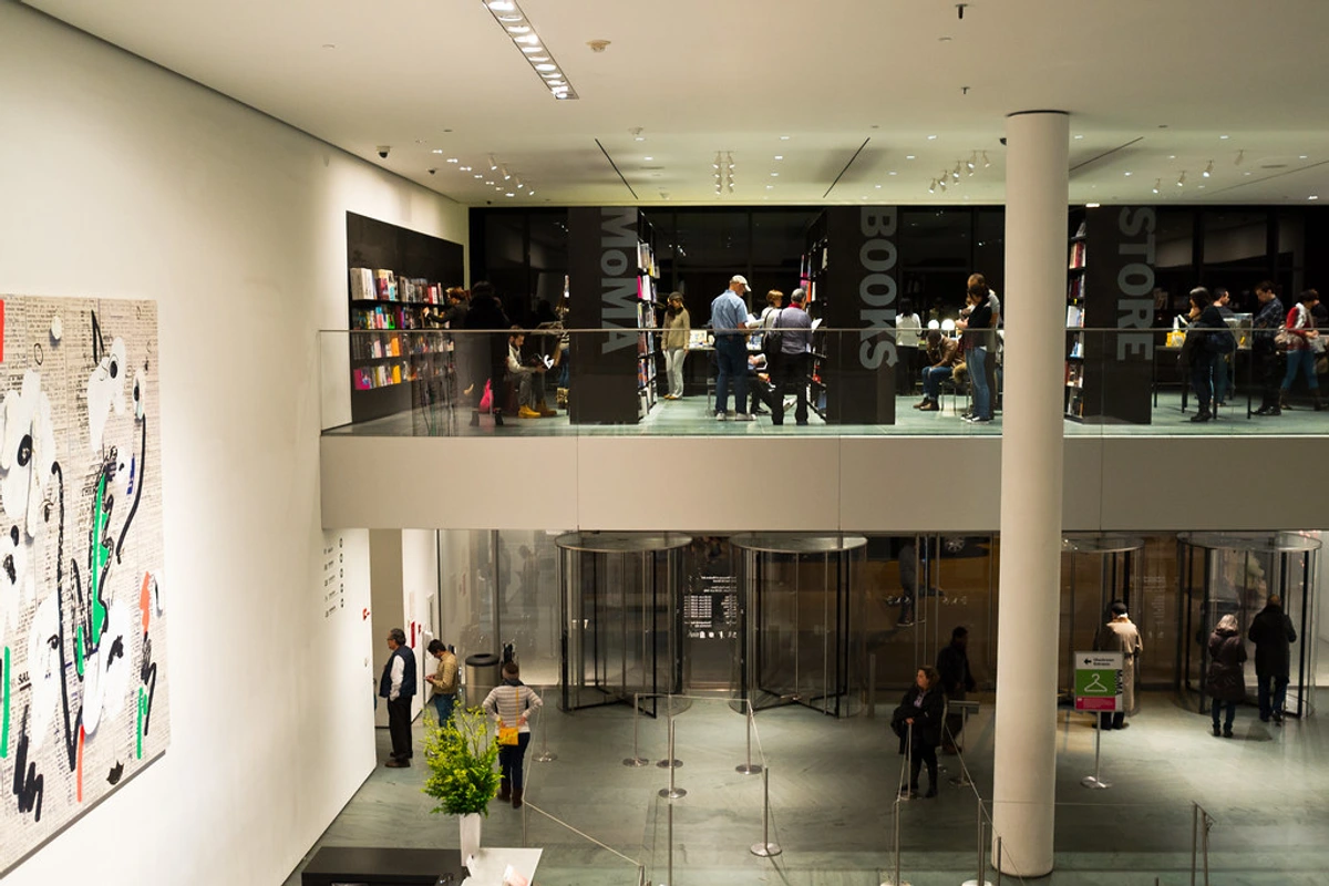 Interior view of the MoMA bookstore and gallery, showcasing bookshelves, artwork, and visitors.