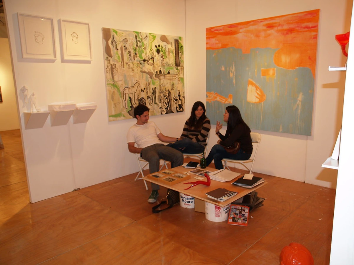 Three people sitting around a table in an art gallery, discussing art.