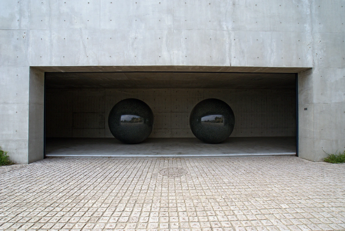 Two large, dark, polished spherical sculptures displayed inside a modern concrete building at Benesse House on Naoshima art island, Japan.