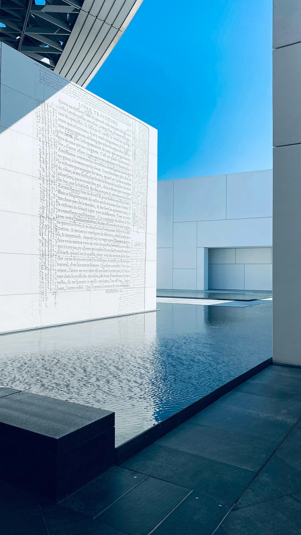 Modern architecture of the Louvre Abu Dhabi museum with a reflective water feature and clear blue sky.