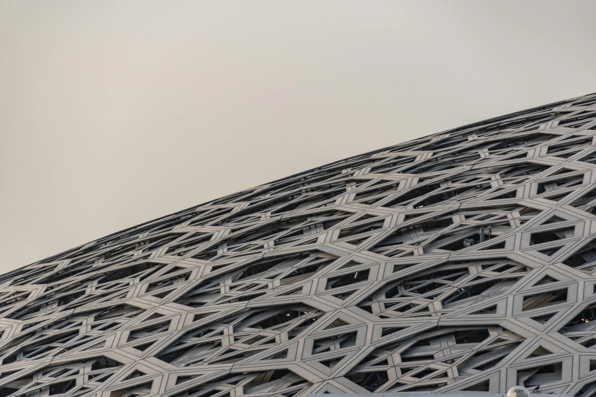 Close-up of the intricate geometric dome structure of the Louvre Abu Dhabi museum, showcasing how light is filtered through architectural glass elements.