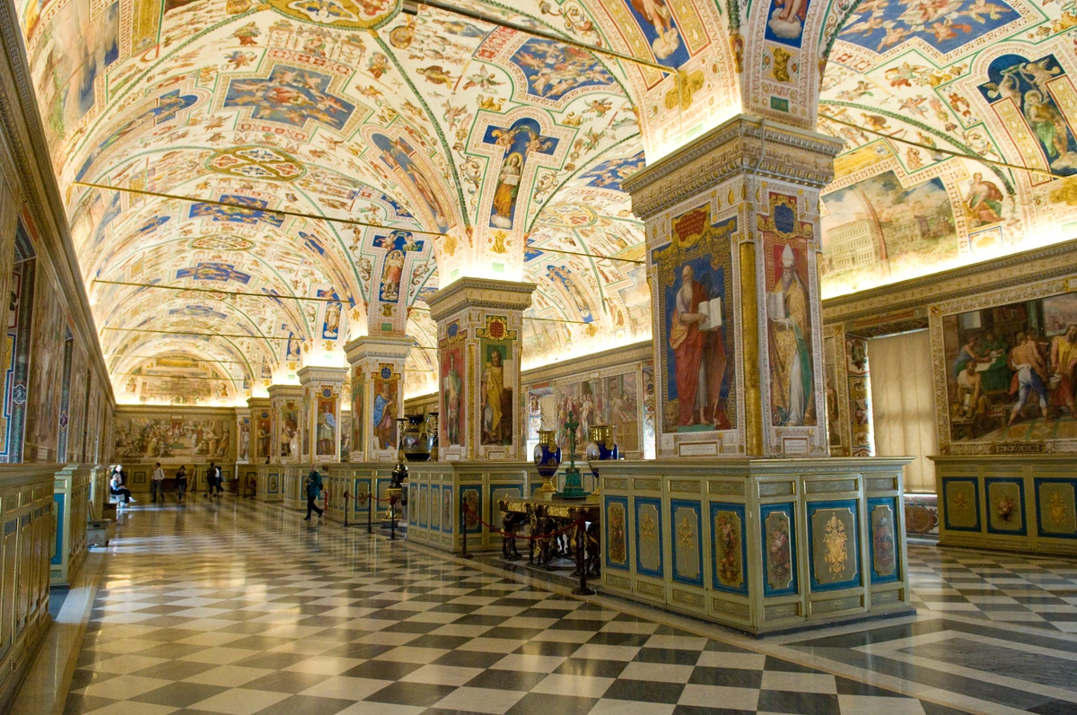 Interior of the Sistine Hall in the Vatican Library, featuring ornate frescoes on the ceiling and walls, and a checkered marble floor.