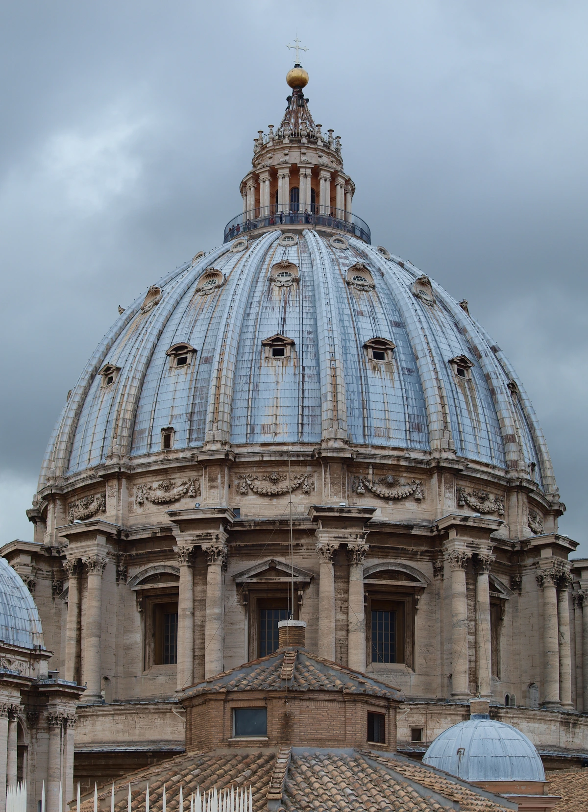 Close-up of the dome of St. Peter's Basilica in Vatican City, showcasing its architectural details and weathered facade under a cloudy sky.