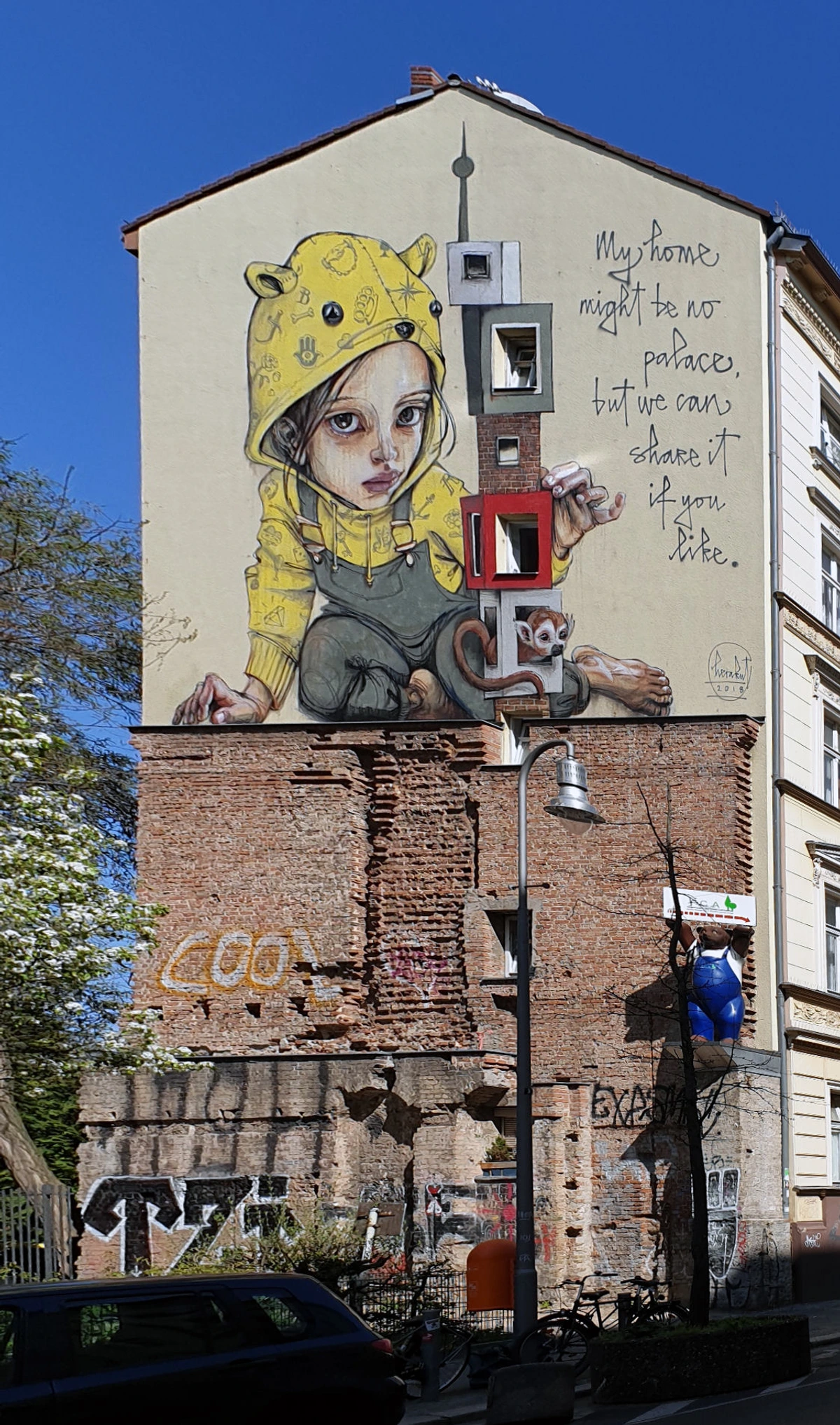 Mural by Herakut in Berlin Kreuzberg depicting a girl in a yellow hoodie holding toy blocks, with text 'My home might be no palace, but we can share it if you like.'