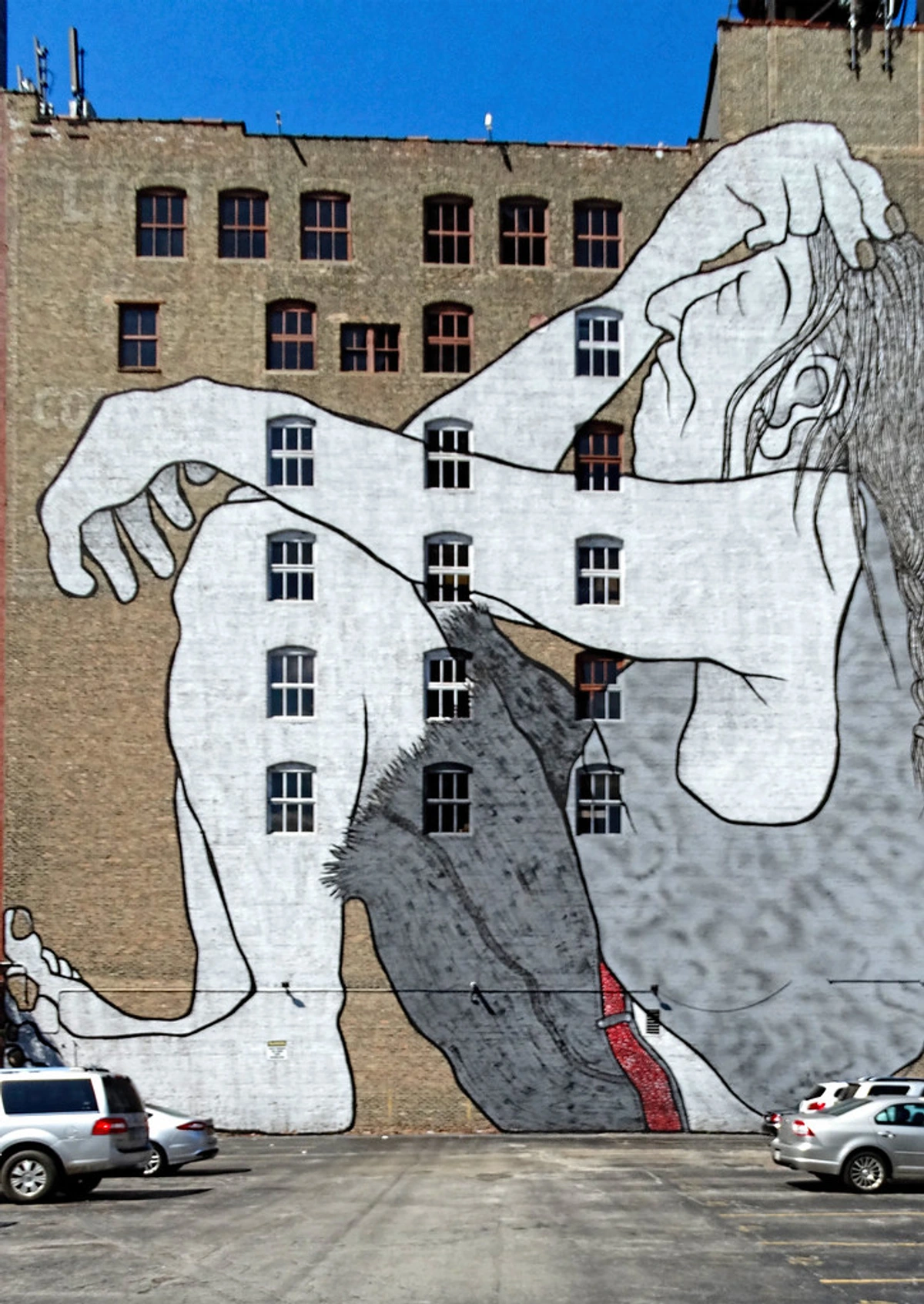 A large-scale mural depicting a Native American figure covers the side of a brick building in Chicago, with windows integrated into the artwork.