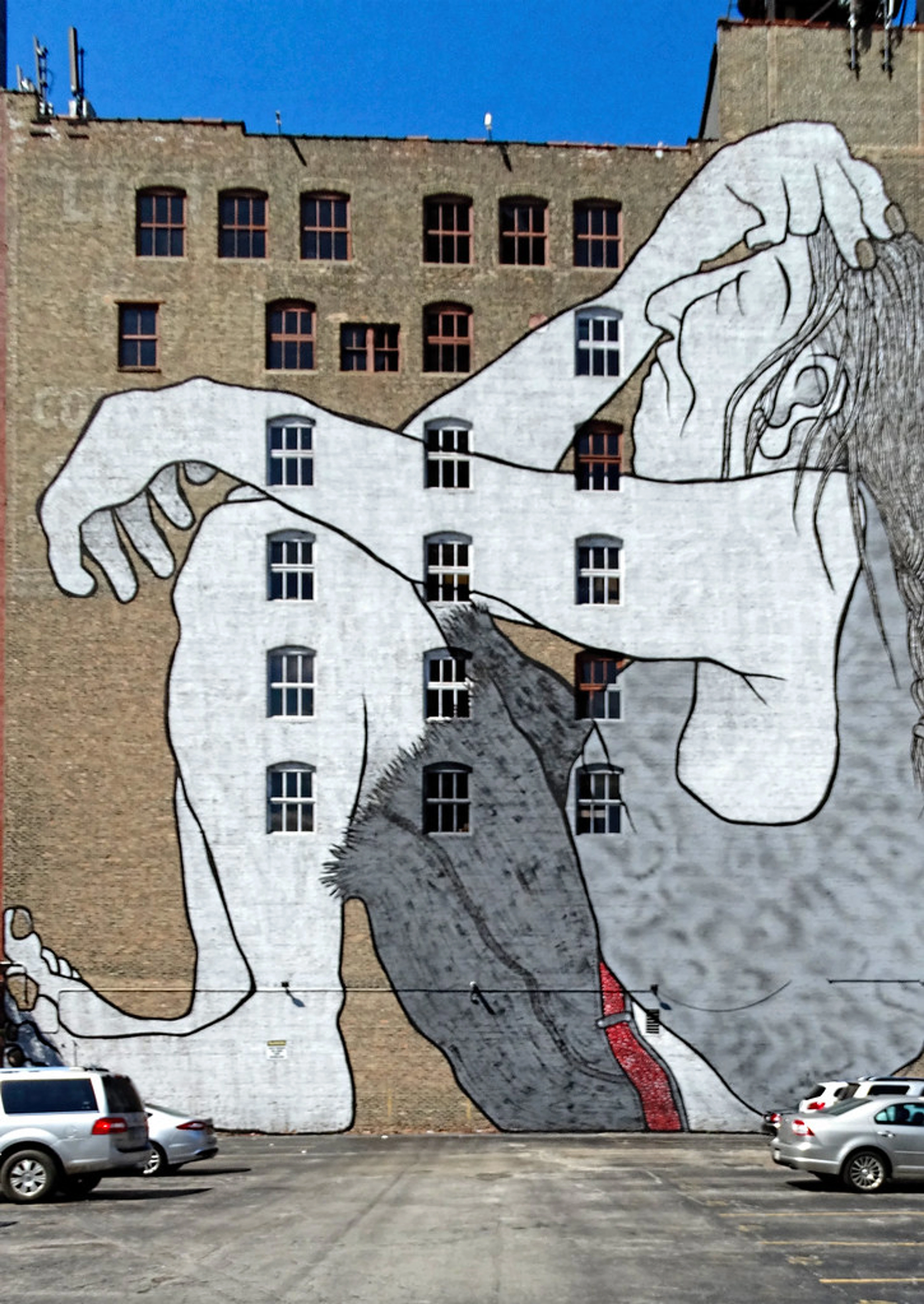 A large-scale mural depicting a Native American figure covers the side of a brick building in Chicago, with windows integrated into the artwork.