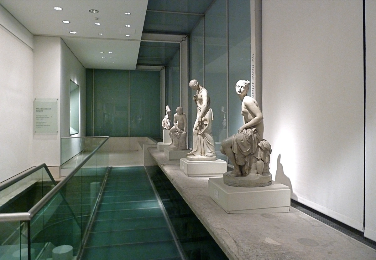 Interior view of the Royal Academy sculpture gallery, showcasing classical marble statues displayed on a raised platform with a glass floor below.