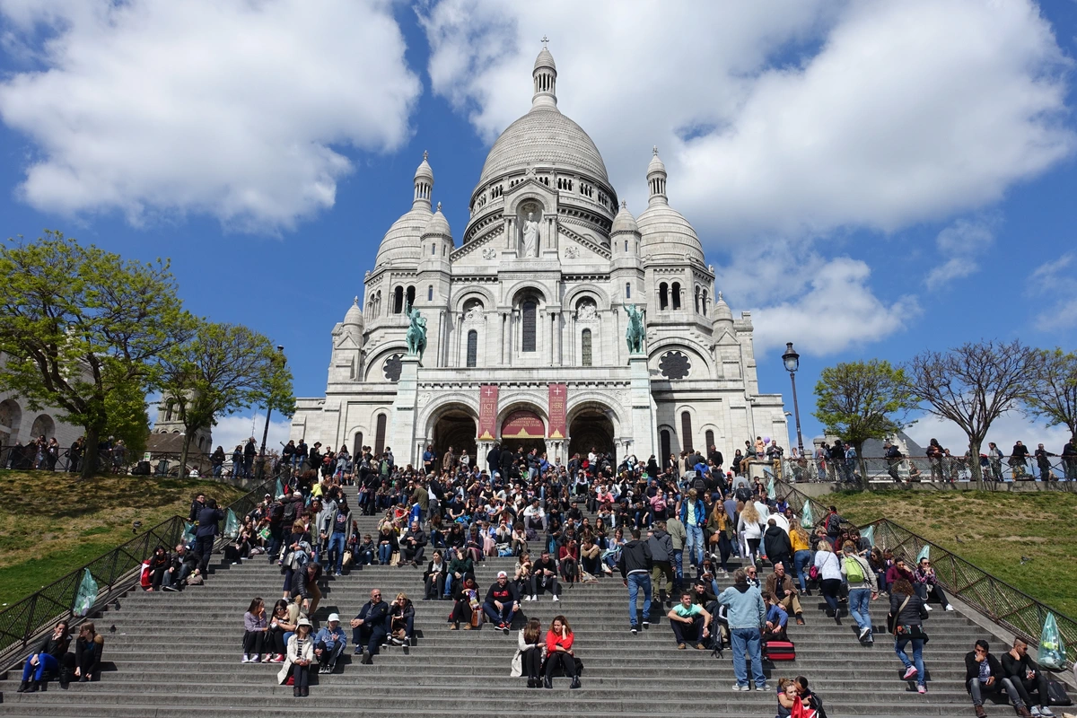 Tourists gathered on the steps of the Sacré-Cœur Basilica in Montmartre, Paris, on a sunny day.