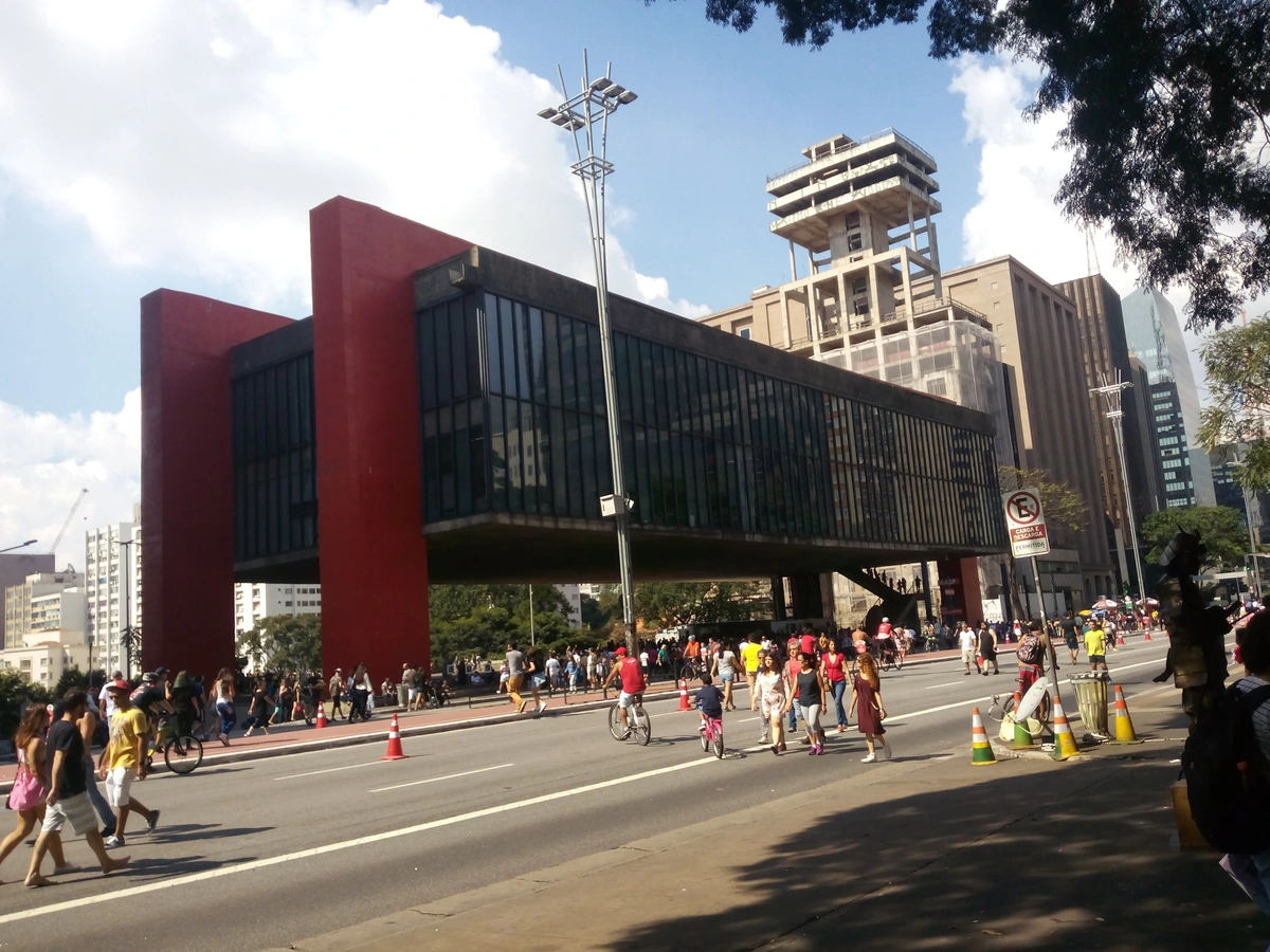 Exterior view of the Museu de Arte de São Paulo (MASP) with Avenida Paulista in the foreground, featuring its iconic red pillars and elevated glass structure.