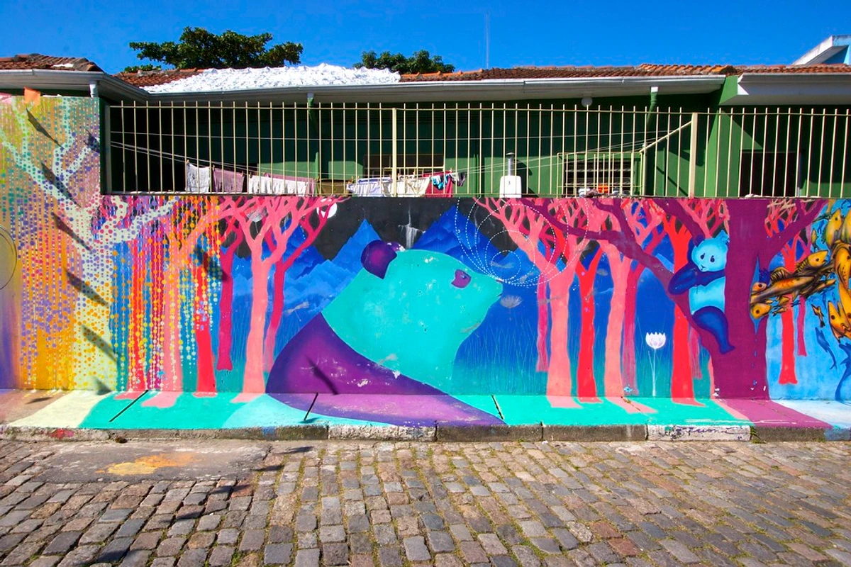 Vibrant São Paulo graffiti mural featuring a large teal and purple panda blowing dandelion seeds in a forest of pink trees.