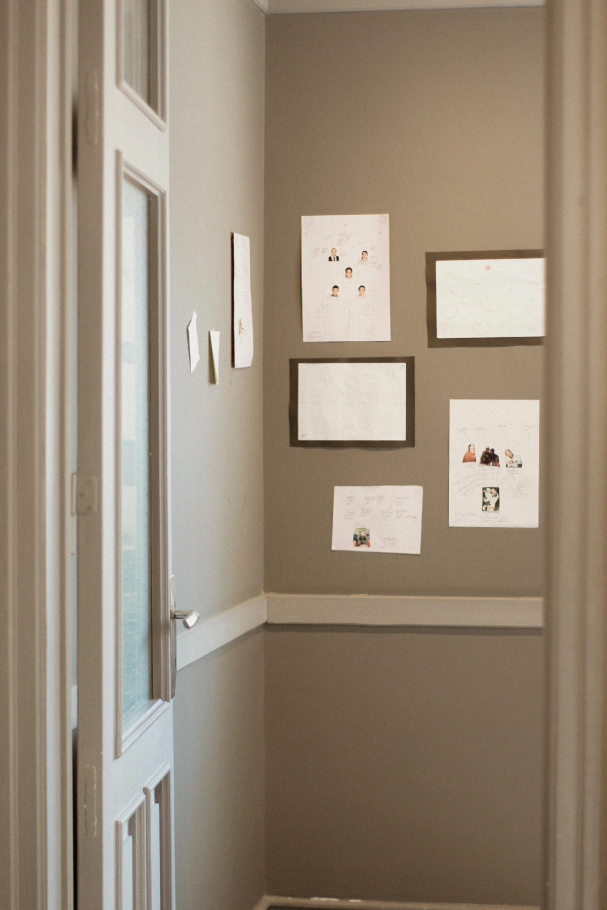 Posters and photos displayed on a beige wall in a narrow apartment hallway next to a white door. The arrangement of frames and bold imagery here suggests a contemporary echo of Art Deco's graphic appeal.