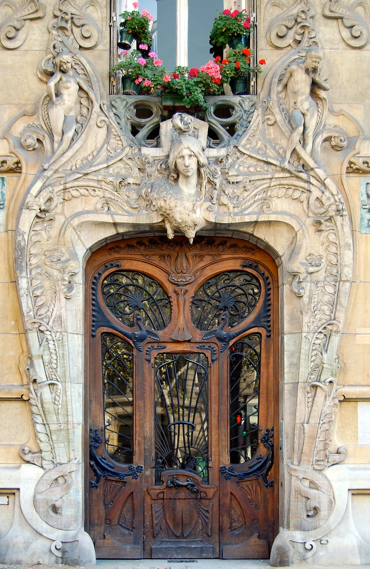 Ornate Art Nouveau doorway in Paris with sculpted figures, floral motifs, and a wooden door with wrought iron details.
