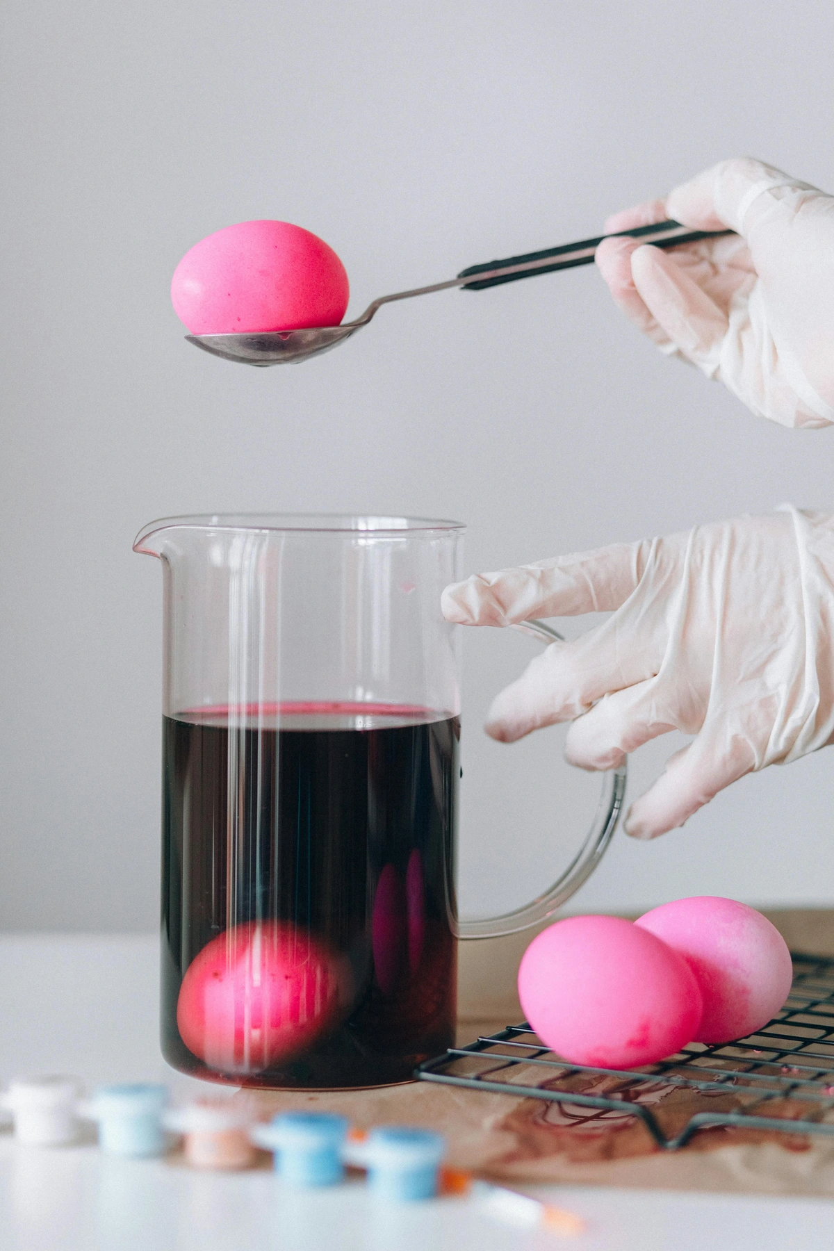 Hand holding stainless steel spoon with pink egg demonstrating egg-dyeing art techniques for beginners