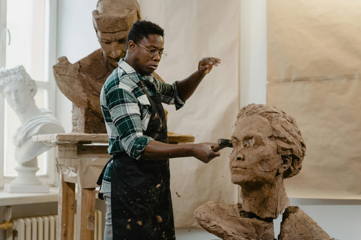 Man hitting clay sculpture with hammer in workshop, artistic creation process