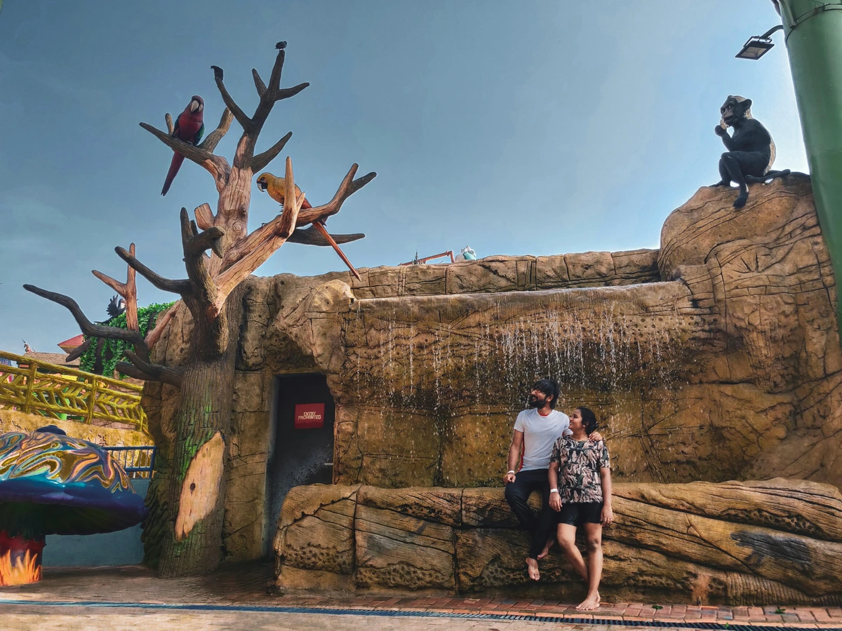 Two people standing in a waterfall surrounded by exotic animals. Artistic natural environment promoting appreciation of culture and nature. Free stock photo.