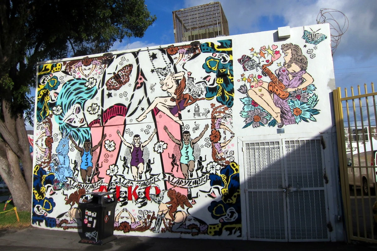 Vibrant Aiko mural at Wynwood Walls, Miami, featuring pop art style figures, butterflies, and flowers.