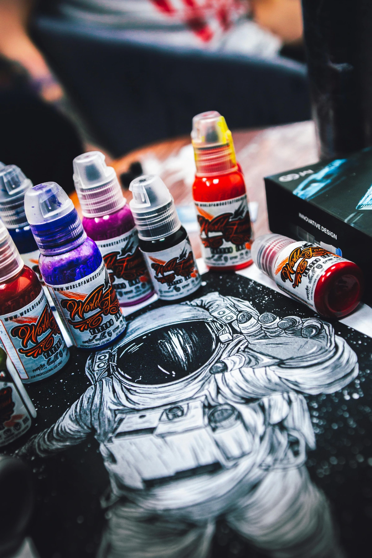 Colorful tattoo ink bottles arranged around a drawing of an astronaut, showcasing vibrant colors for artistic use.