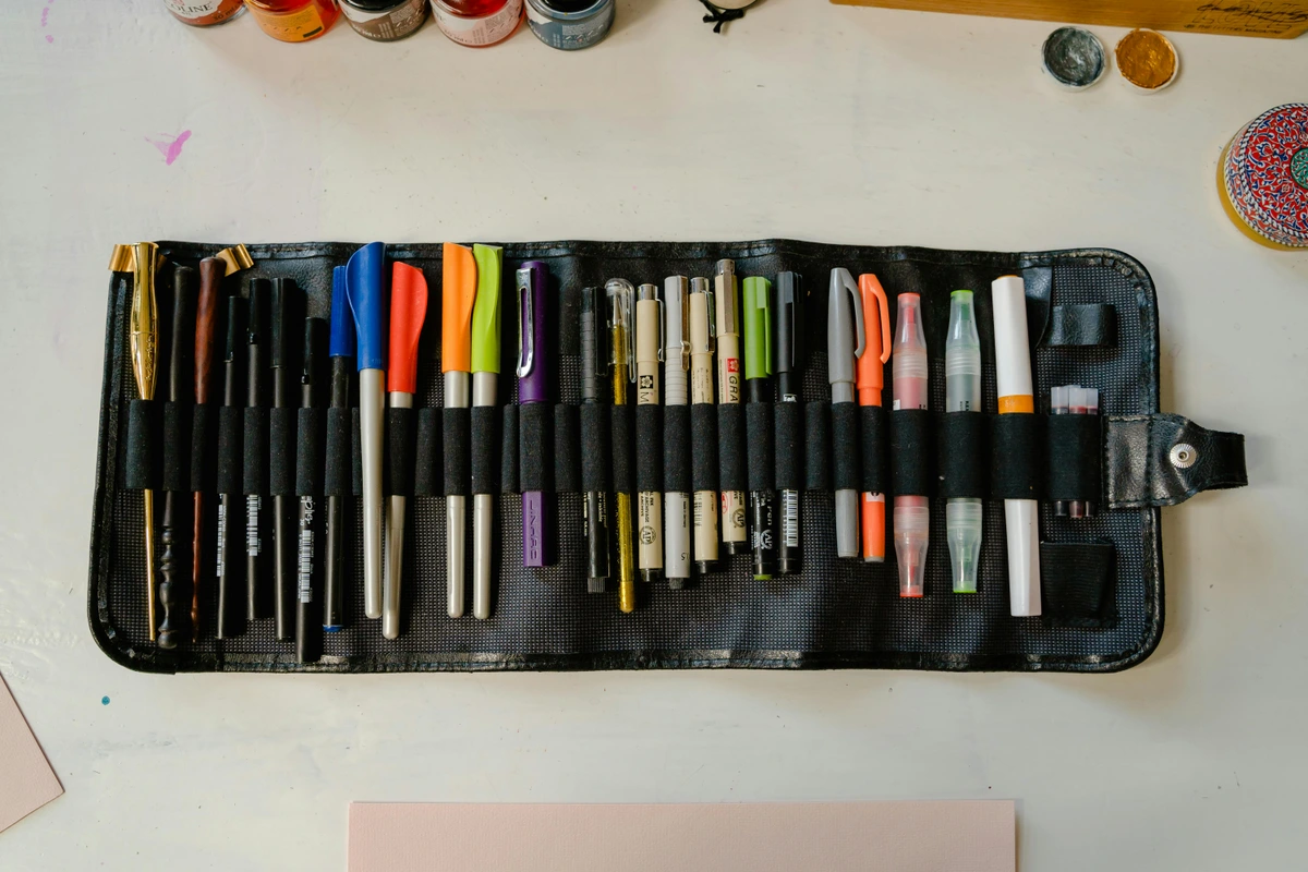 A black roll-up case filled with various colorful markers and pens, laid out on a white table.