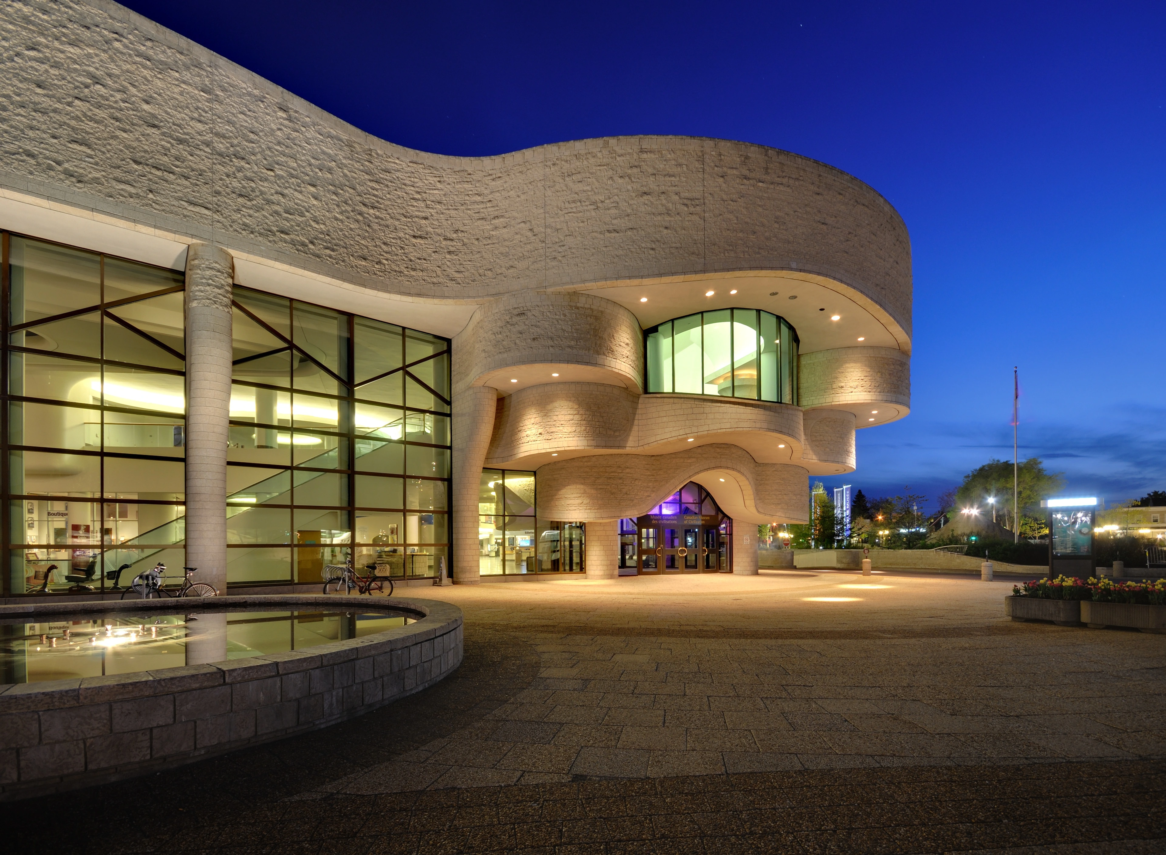 The Canadian Museum of History in Gatineau, Quebec, at dusk, showcasing its distinctive modern architecture with curved stone and glass facades.