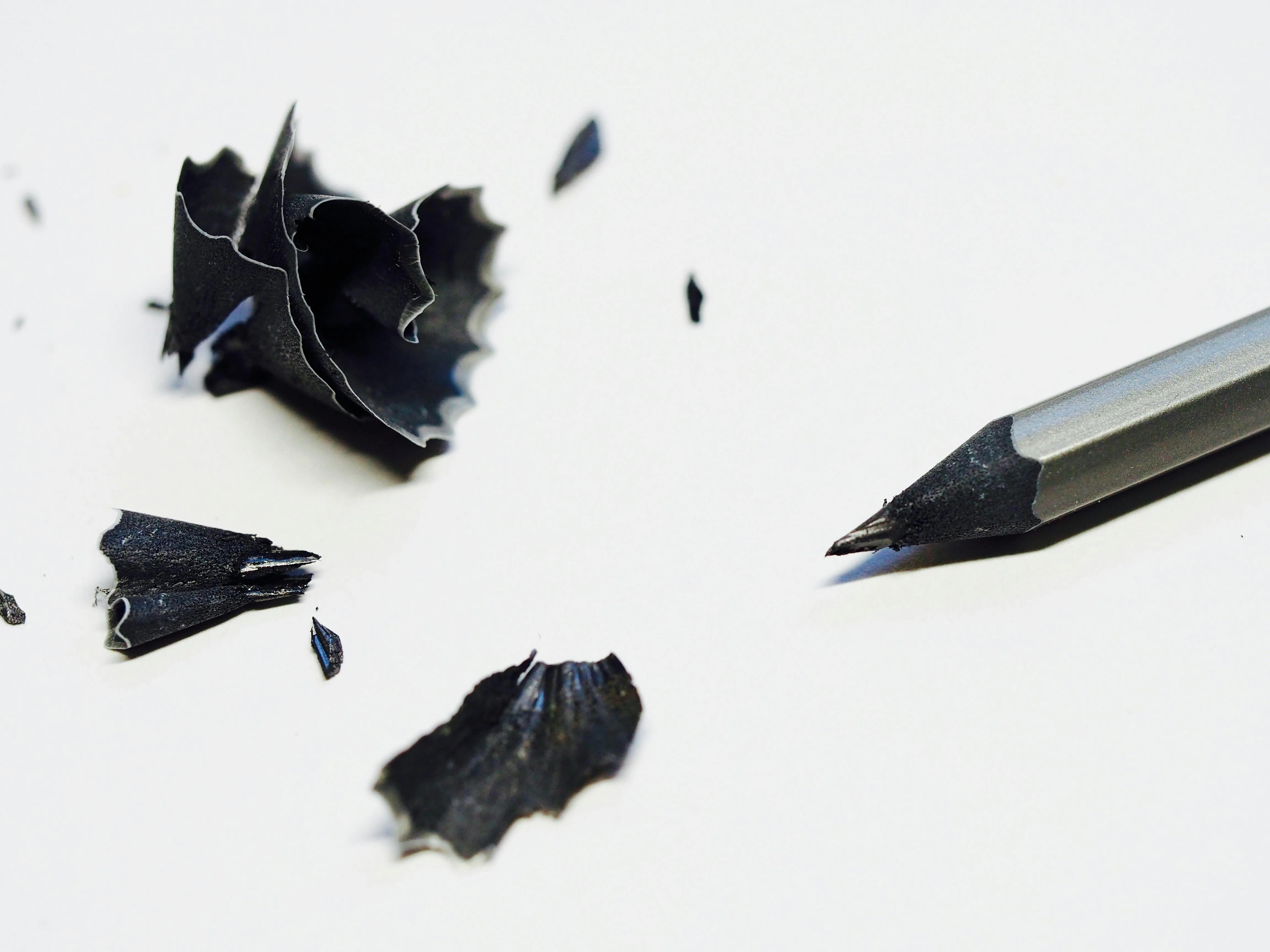 Close-up of a sharpened graphite pencil next to black pencil shavings on a white background.