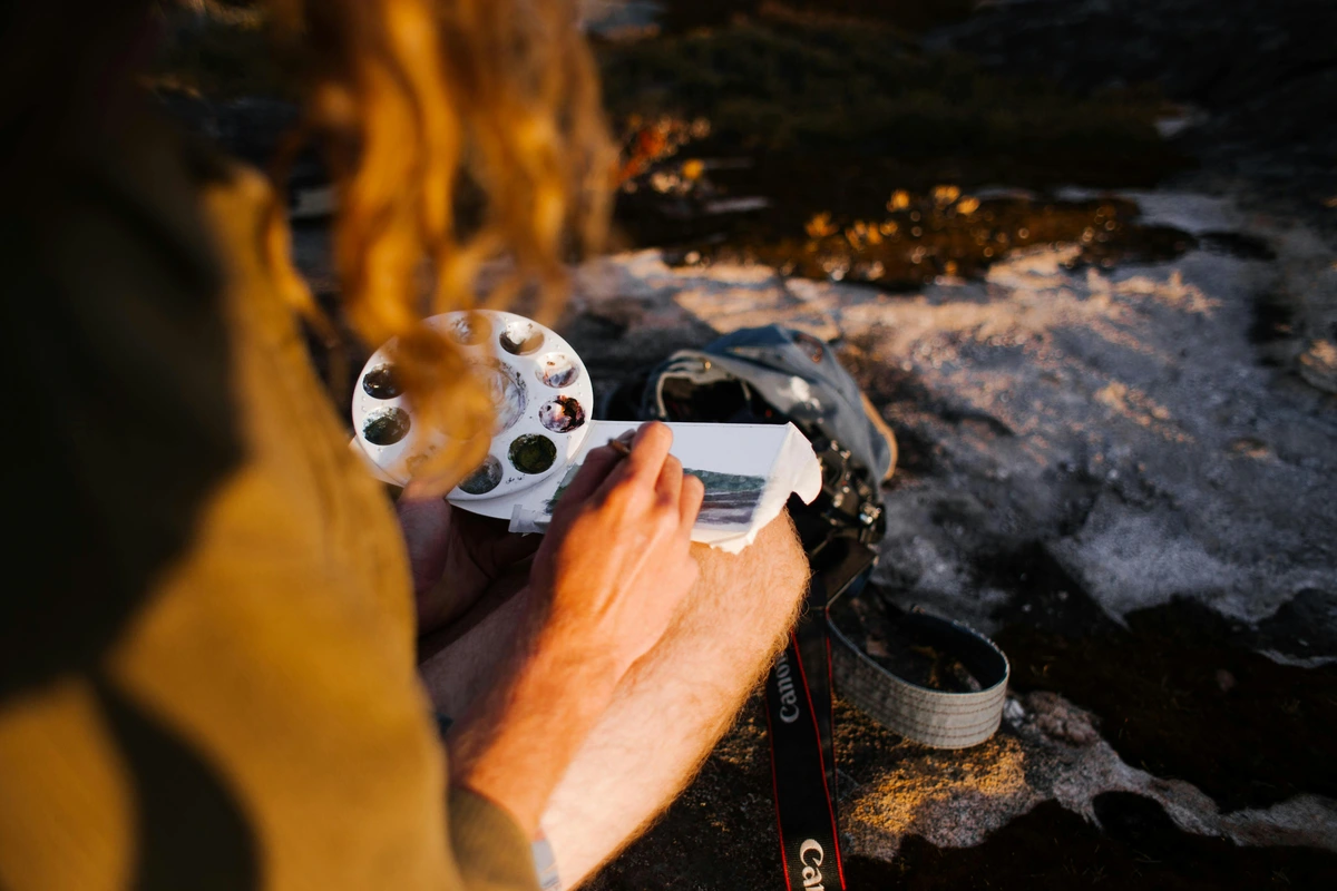 Man painting a tiny watercolor in plain-air at sunset, a small, intimate moment of creation, much like the focus required for a still life.