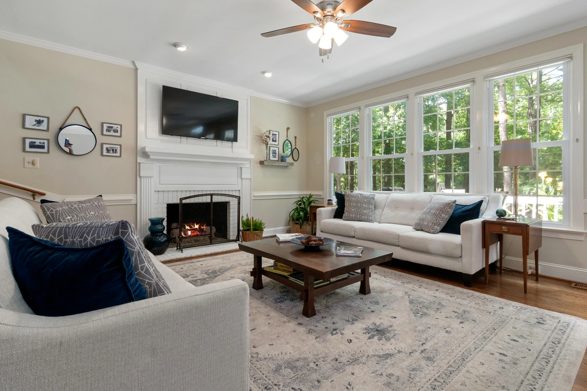 Cozy living room with a white couch, coffee table, and fireplace, featuring large windows with natural light.