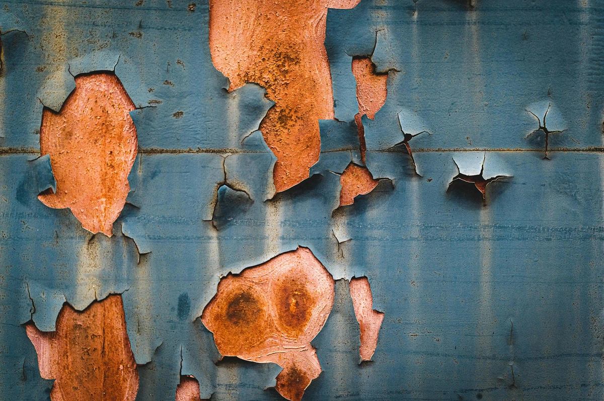 Close-up of peeling blue paint revealing rusty metal texture underneath, showcasing common paint film problems.