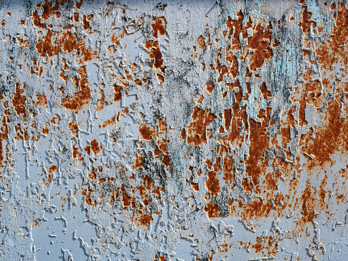Close-up texture of peeling blue paint revealing rust and metal underneath, showing signs of decay and weathering.