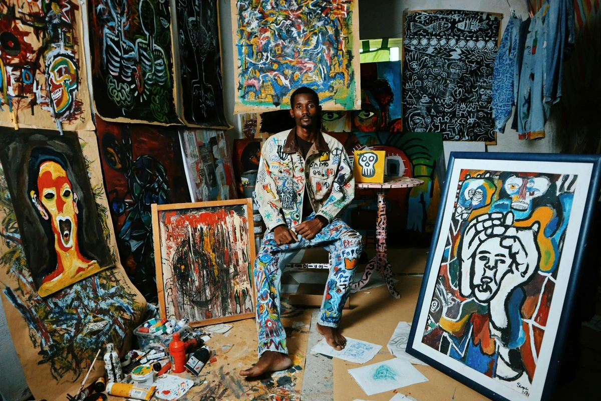 Artist surrounded by paintings in a creative studio environment with art supplies, showcasing the process of art creation for art buying considerations.