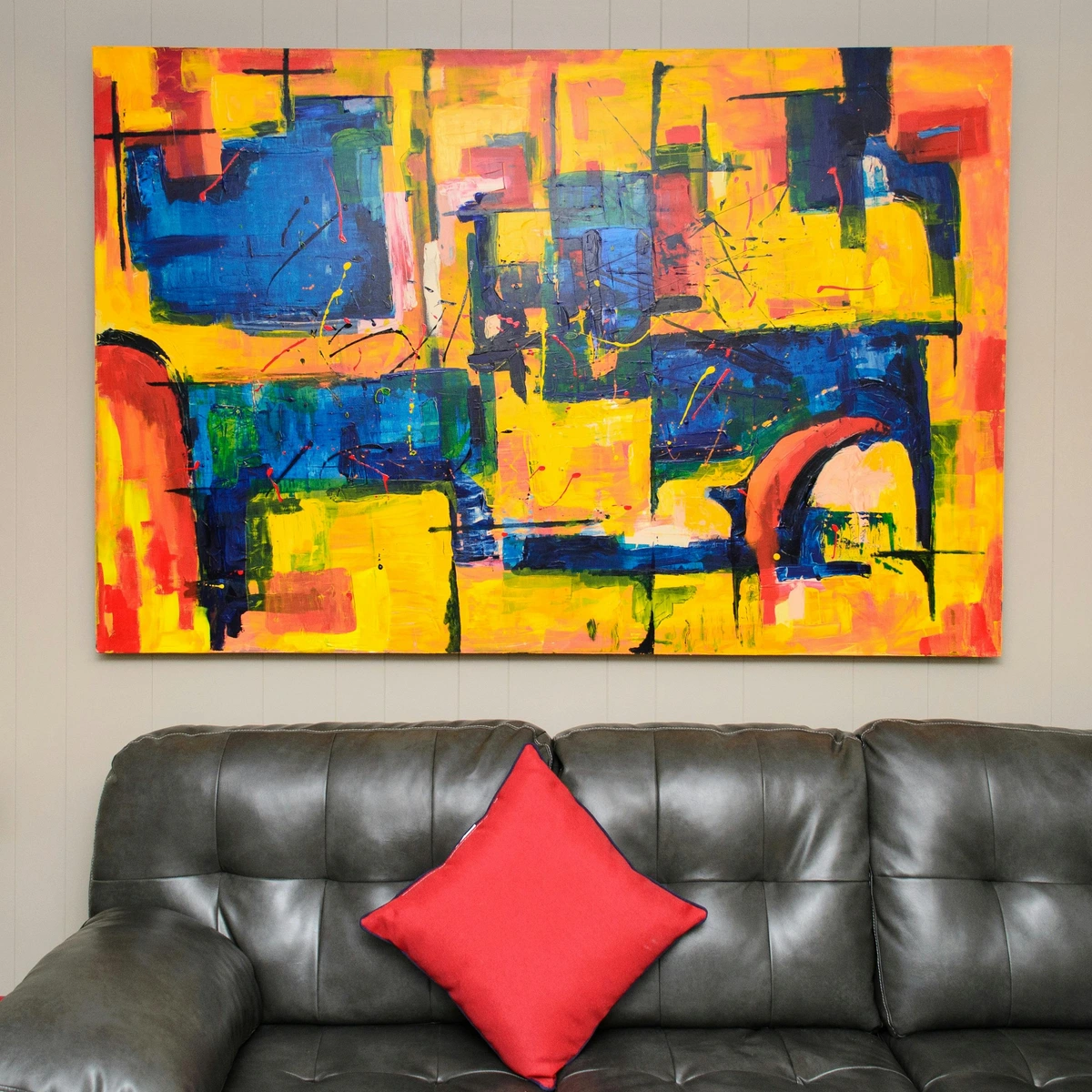 Abstract color painting on white painted wall above a leather couch with a red pillow
