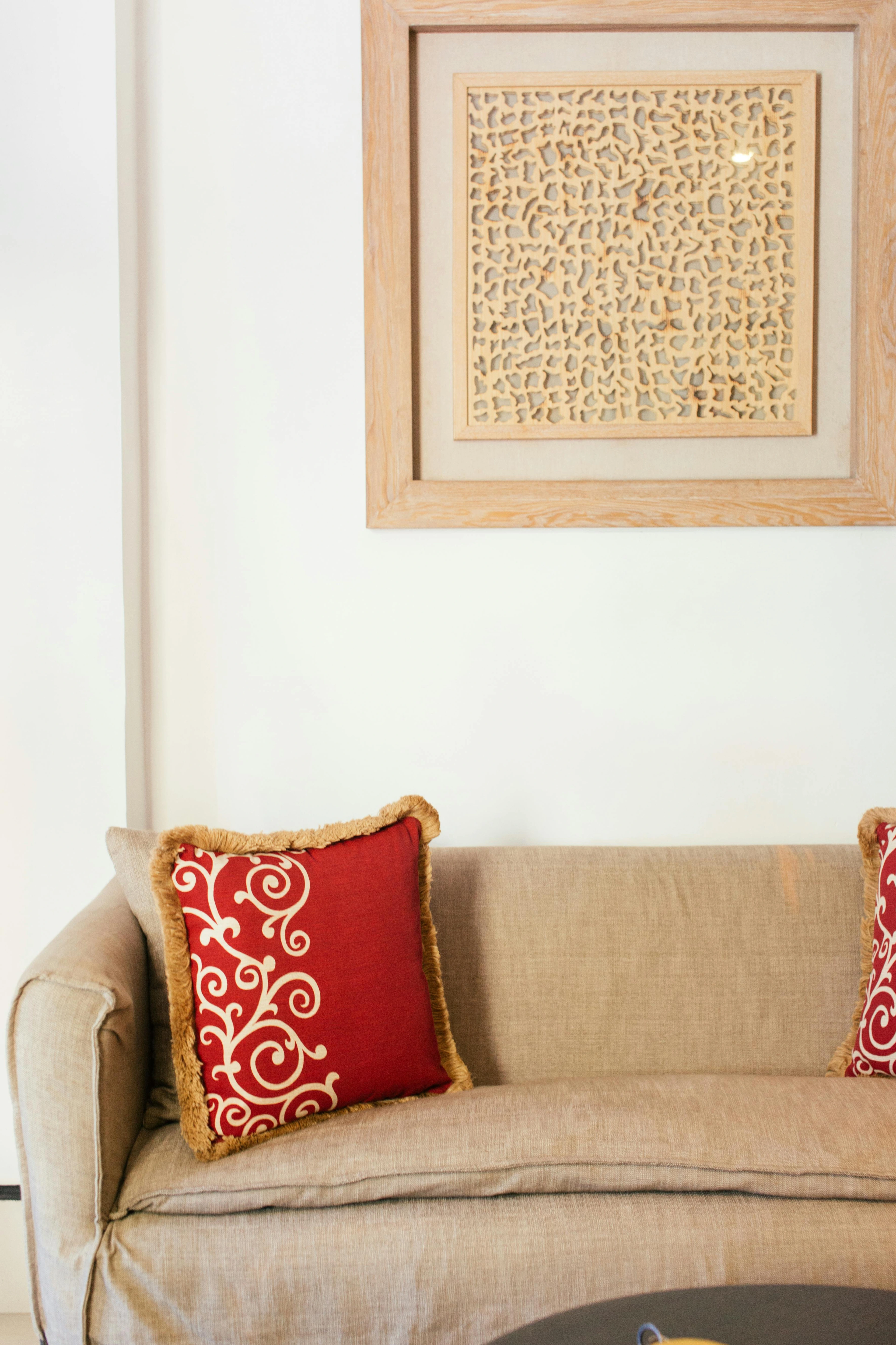 A close-up of a sofa with red decorative pillows and a framed woodcraft hanging on the wall above it, showcasing warmth and texture in home decor.