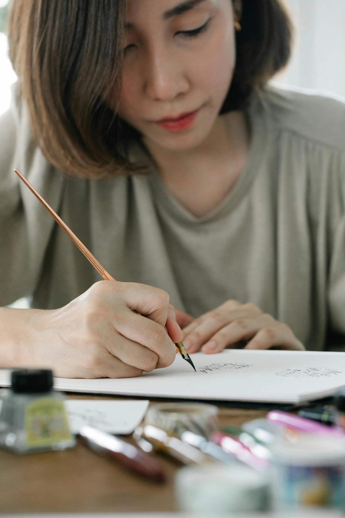 Woman practicing calligraphy in a notebook using an ink pen, showcasing artistic technical mastery in handwriting lettering art.
