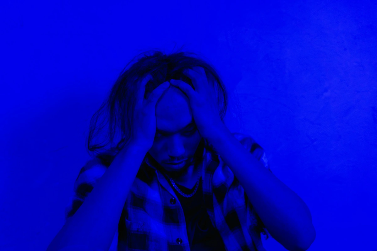 A man expressing anxiety and existential dread with disheveled hair, set against a bleak blue background, artistic emotional portrait.