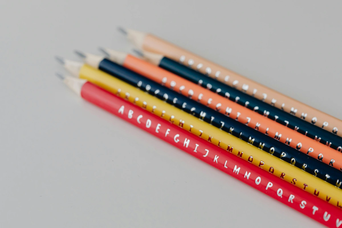 Close-up of colored pencils with alphabet letters imprinted on them, arranged on a white surface.