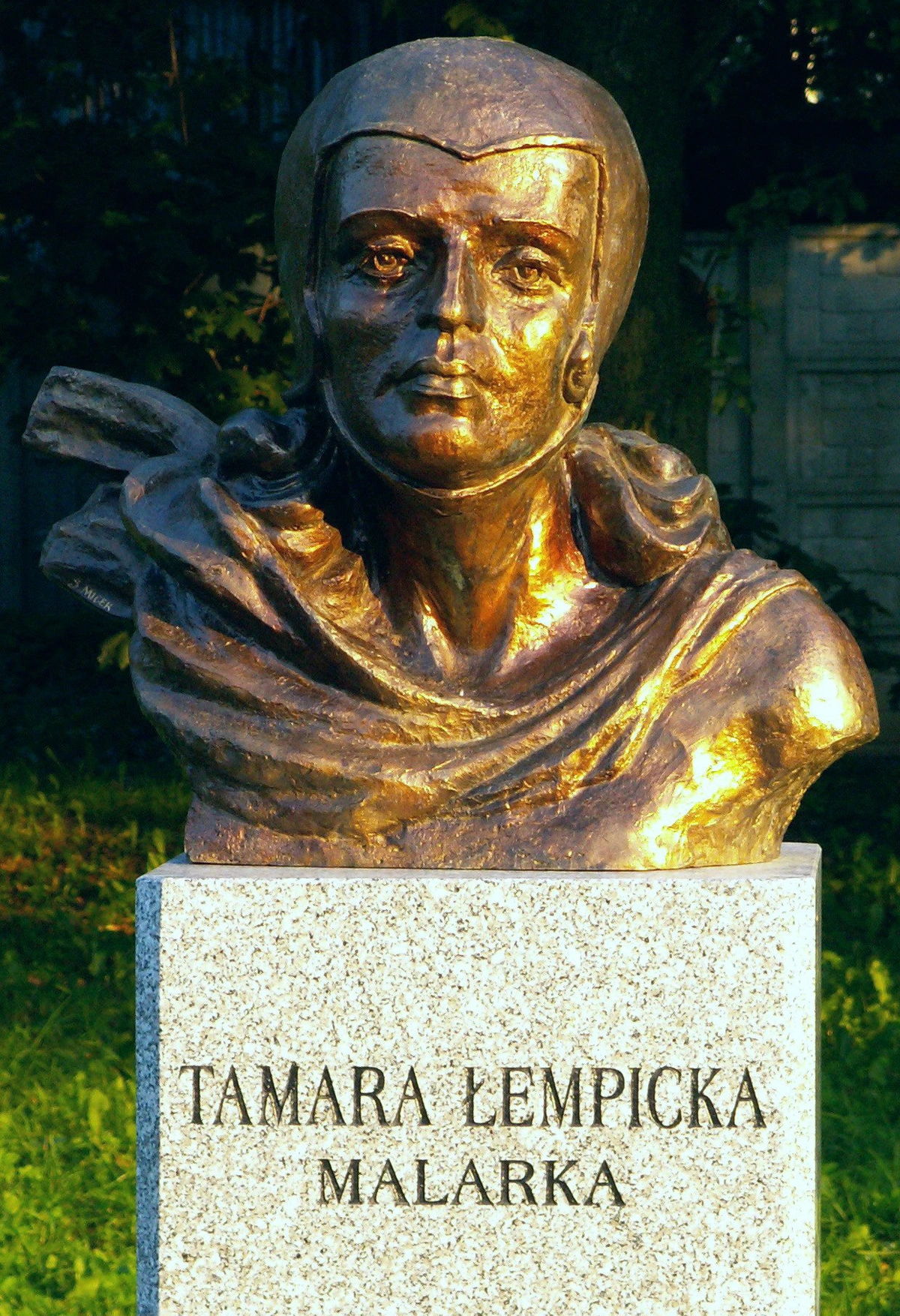 Bronze bust sculpture of famous Art Deco painter Tamara Łempicka, inscribed 'Tamara Łempicka Malarka', displayed outdoors.