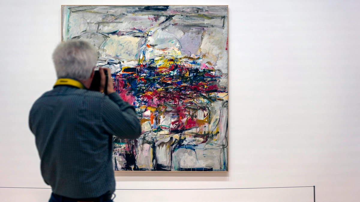 Man photographing Joan Mitchell's abstract painting 'City Landscape' in a museum gallery.