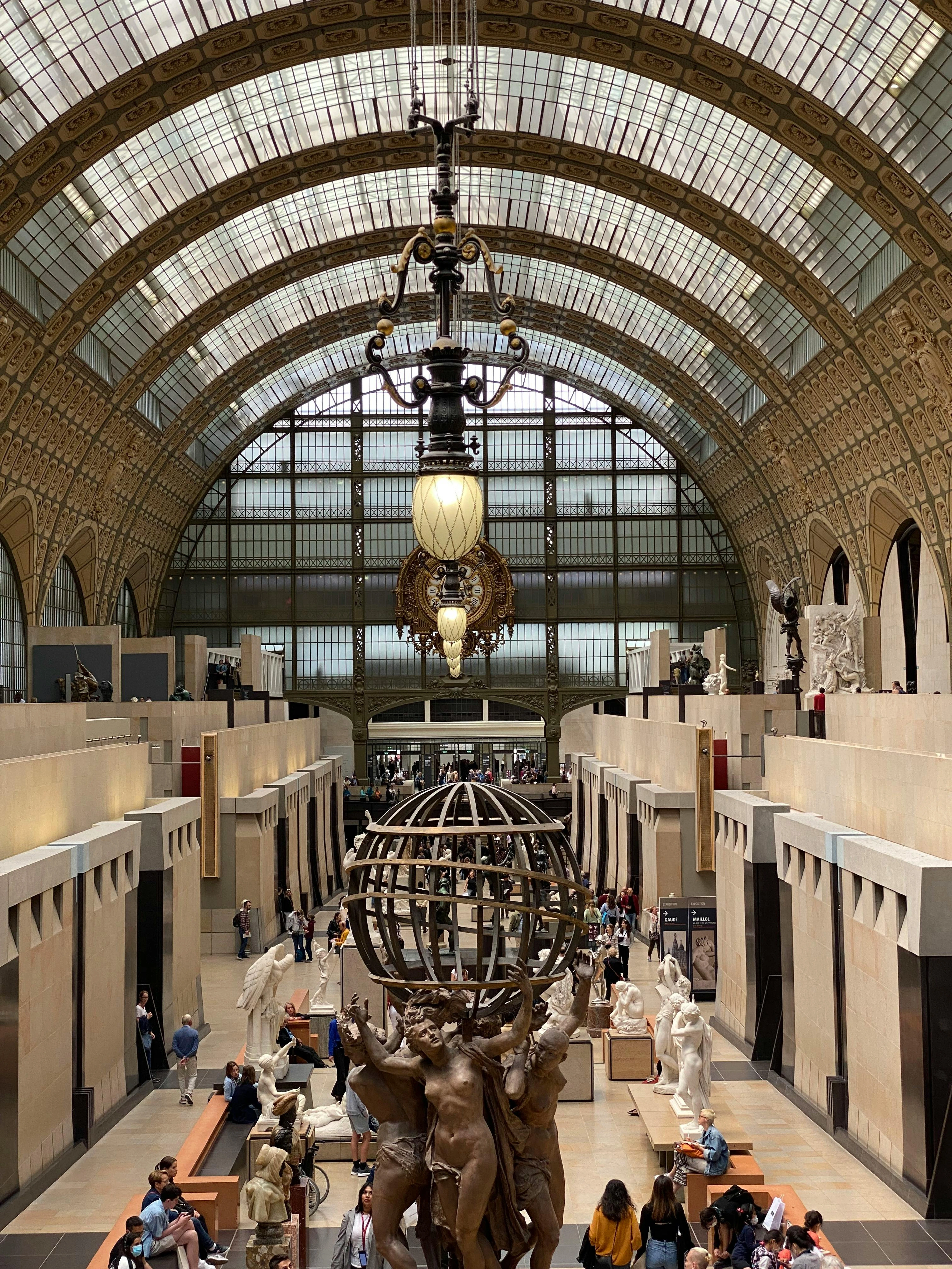 Interior of the Orsay Museum in Paris, featuring the grand hall with its glass ceiling, a large globe sculpture, and numerous statues.