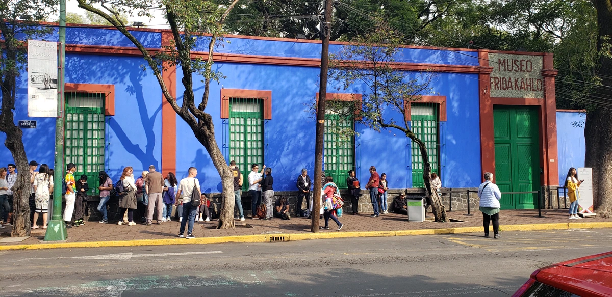 Exterior view of the vibrant blue Museo Frida Kahlo (The Blue House) in Coyoacan, Mexico City, with visitors waiting outside.