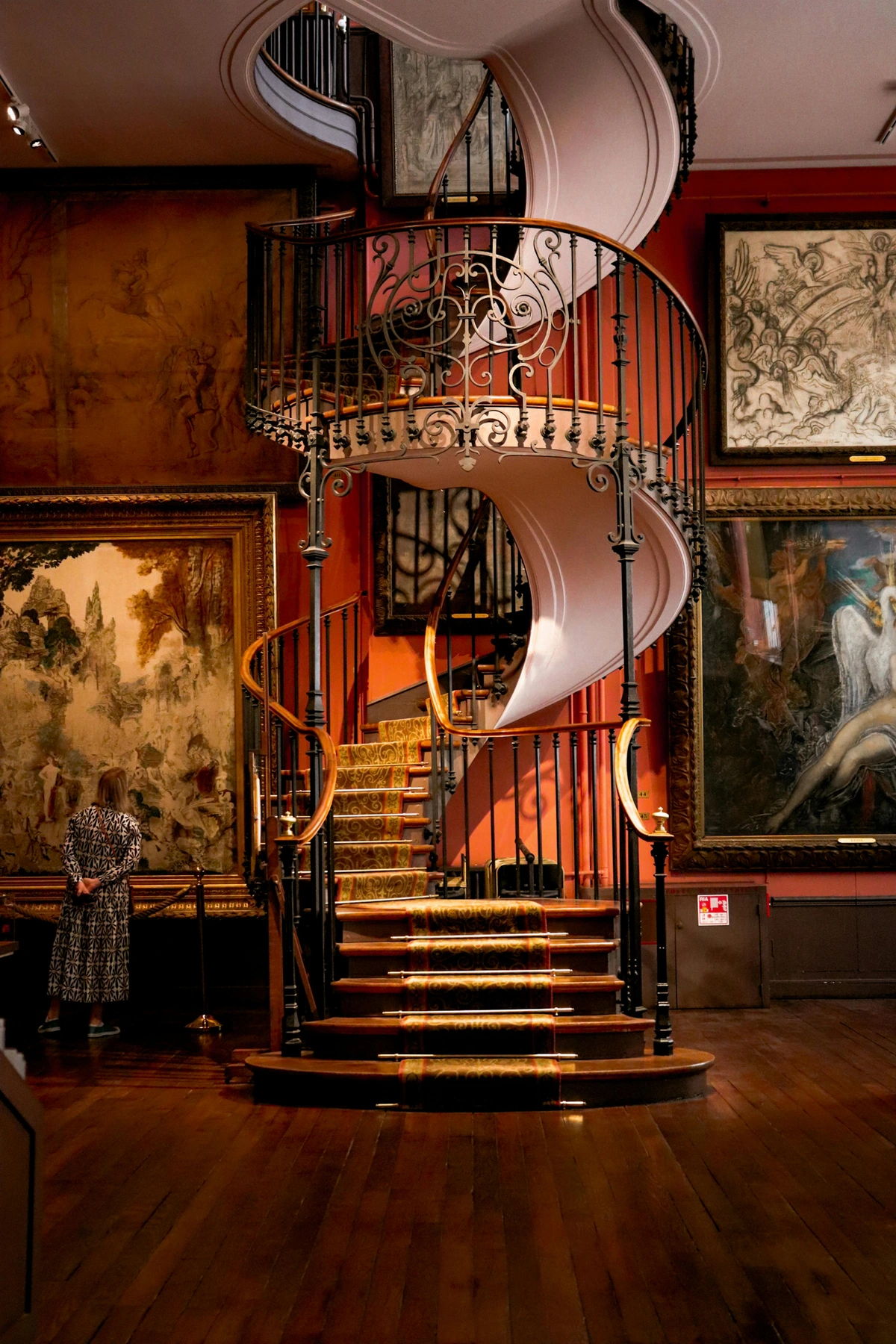 A spiral staircase in a museum with paintings on the walls, featuring ornate railings and carpeted steps.