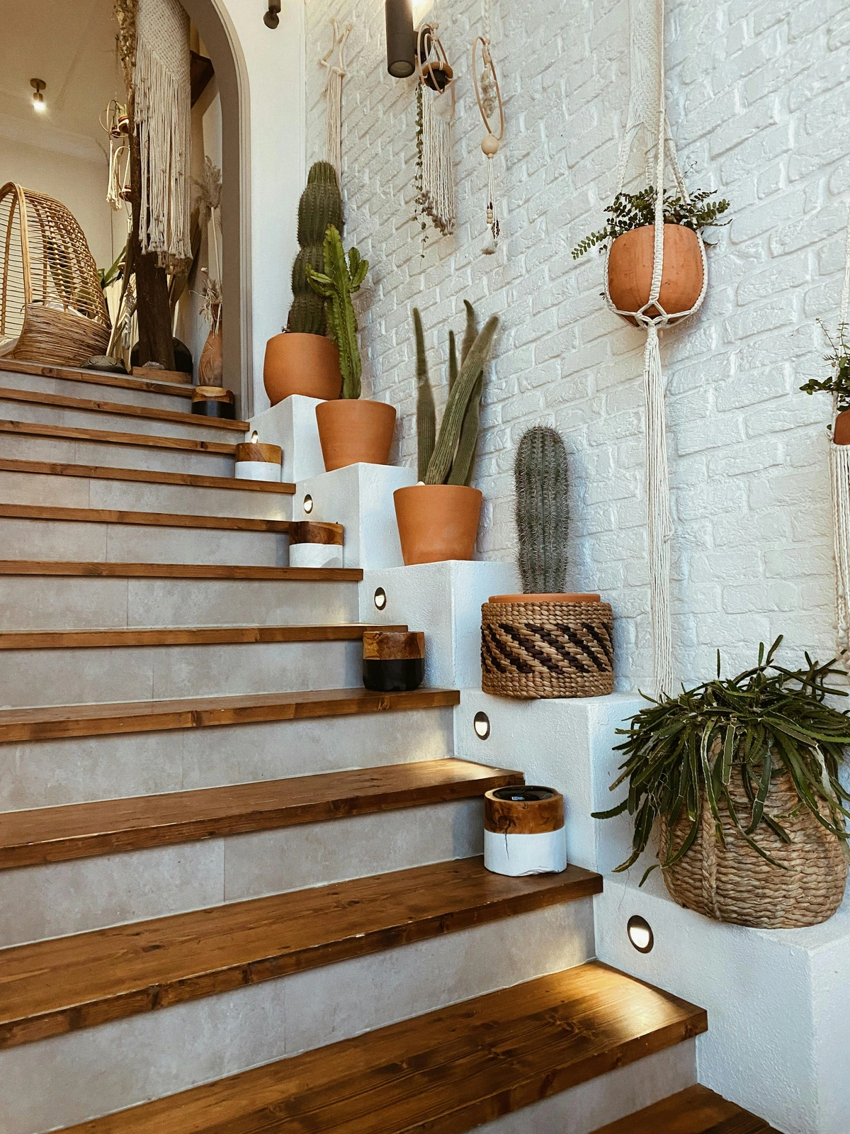Wooden staircase with a gallery wall of potted cacti and hanging plants, decorated in a bohemian style.