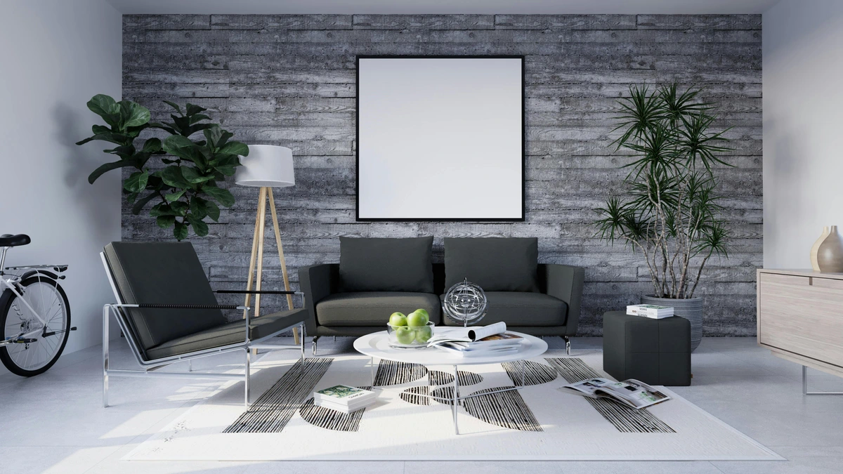 Modern living room with a concrete wall featuring a large blank picture frame, dark grey sofa, armchair, and a round coffee table with books and decorative items.