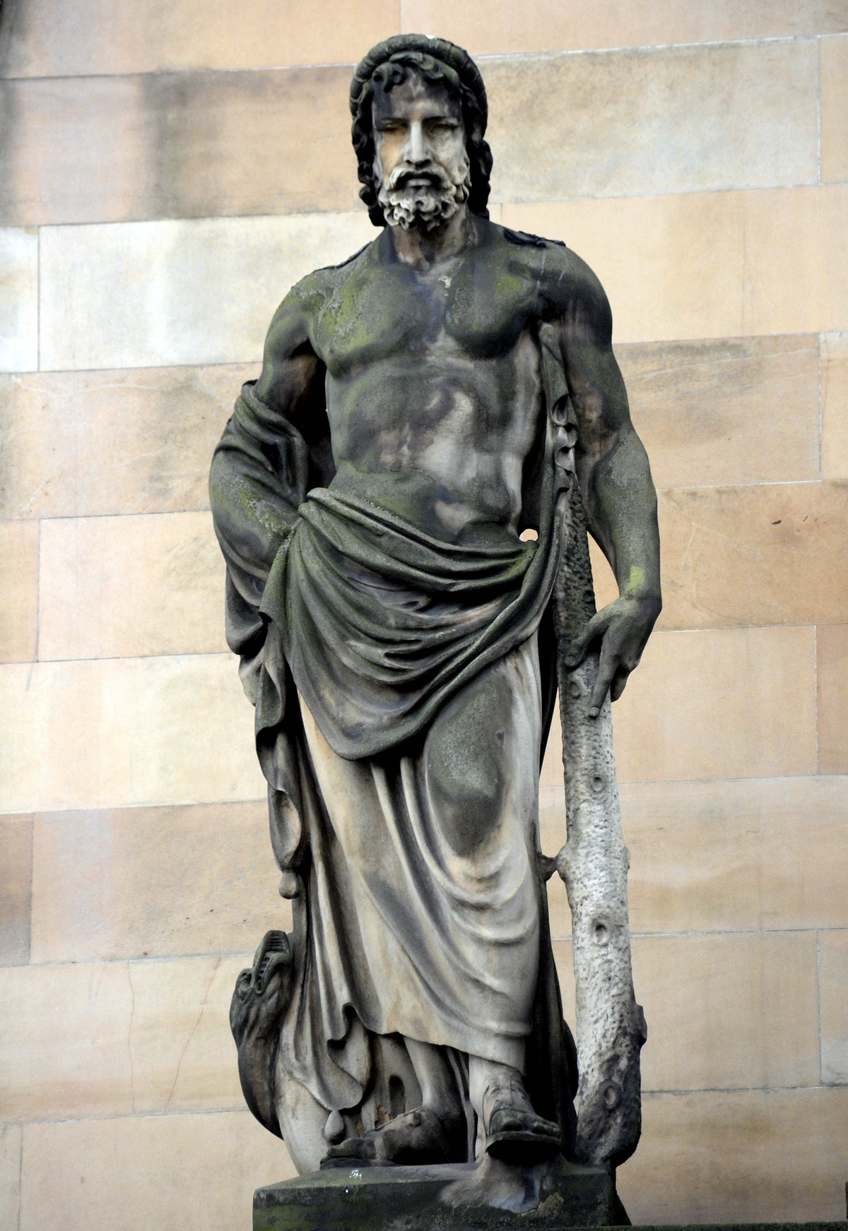 Statue of Asklepios, the Greek god of medicine, depicted as a muscular man holding a staff, with moss and weathering on the stone.