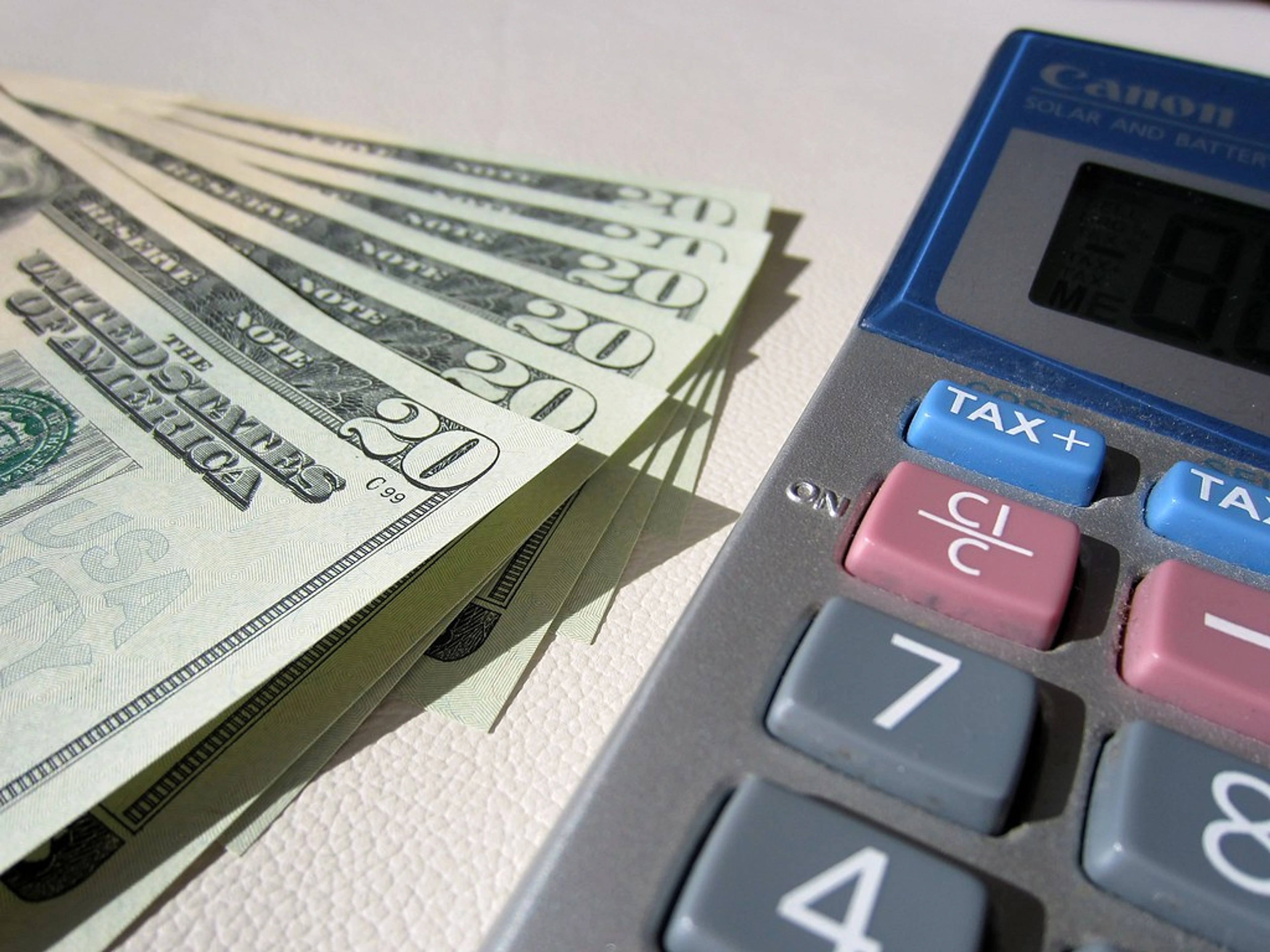 Stack of twenty-dollar bills next to a calculator, symbolizing budgeting and financial management for a freelance artist.