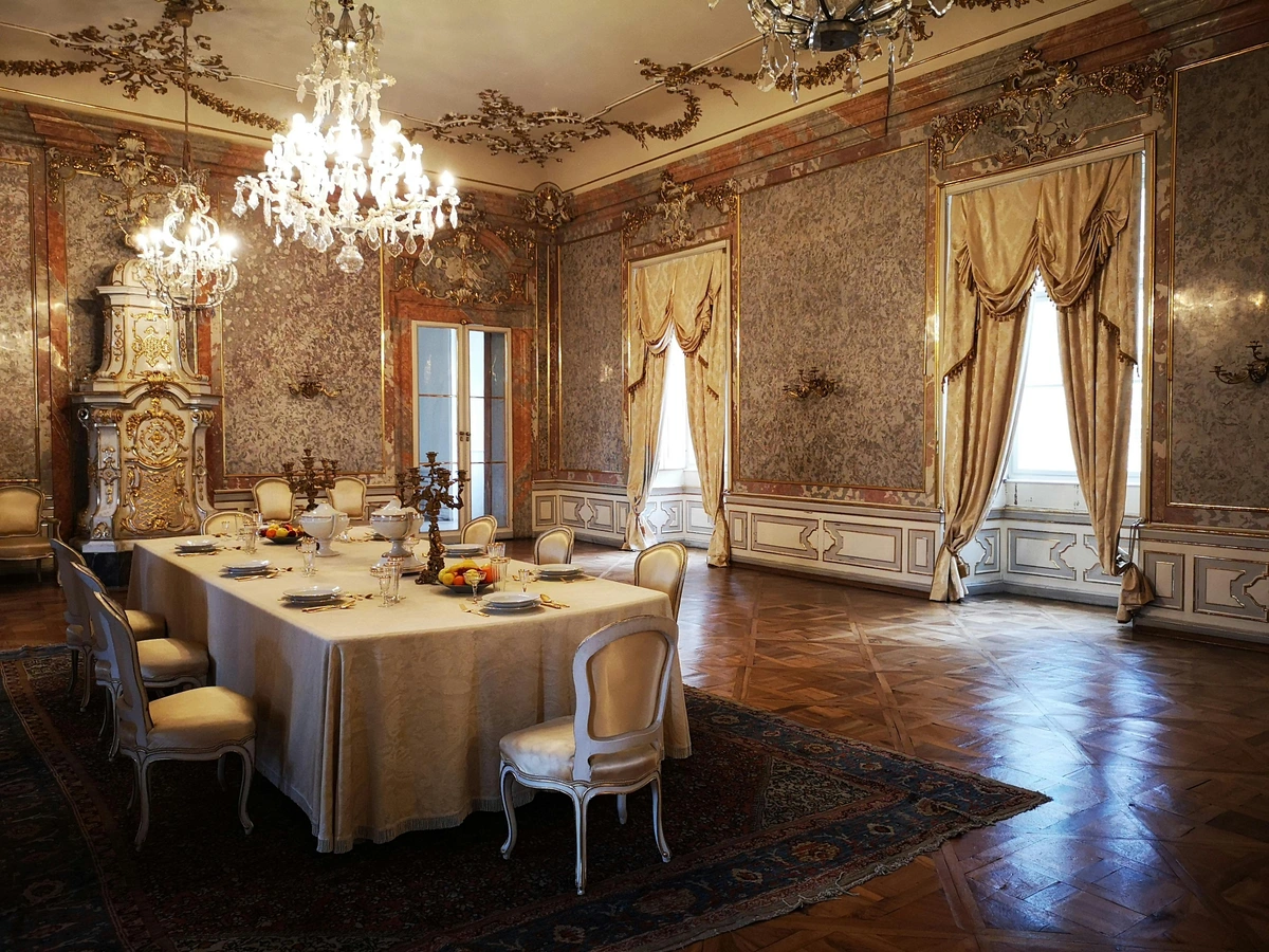 Elegant dining setting in a luxurious ballroom with a table set for a formal meal, featuring crystal chandeliers and ornate decor.